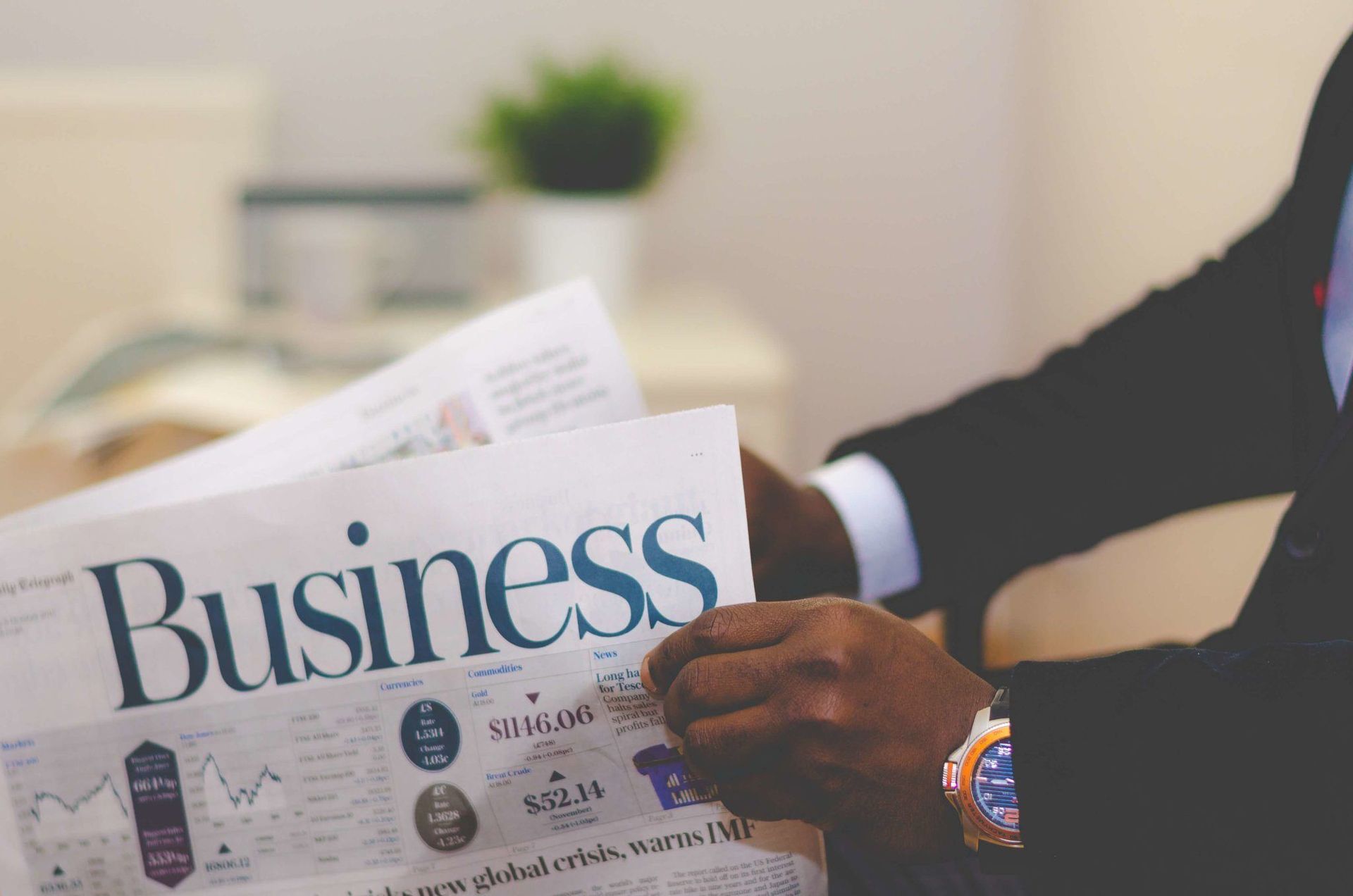 Person reading a Business newspaper at a desk, with a blurred plant in the background