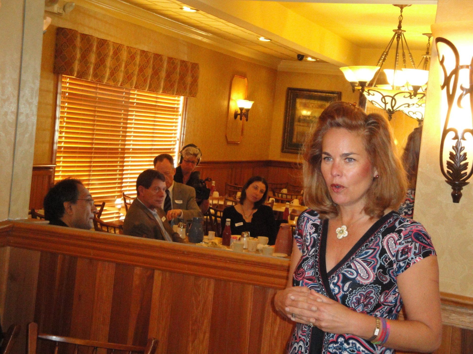A woman stands in front of a group of people in a restaurant