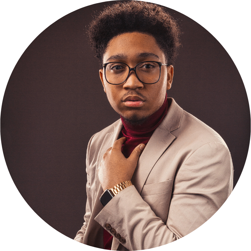 Young Black man in a blazer and glasses, adjusting his red turtleneck, brown background.