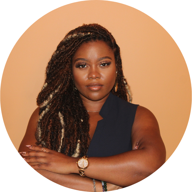 Woman with braided hair, arms crossed, wearing a navy top and gold watch, in front of an orange wall.