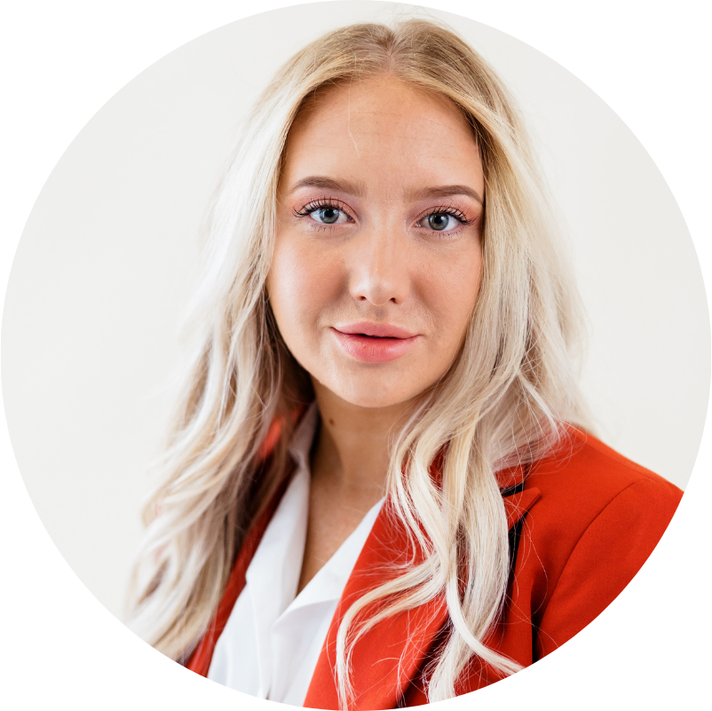 Blonde woman in orange blazer, white shirt, and light background, smiling.