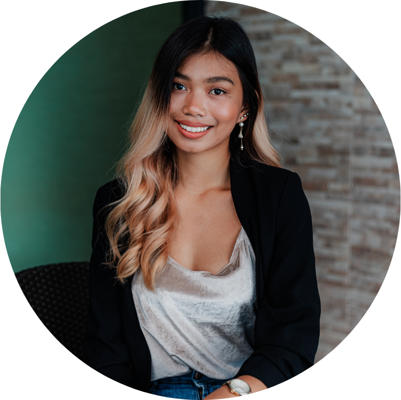 Woman with ombre hair wearing a black blazer, silver top, and jeans, smiling indoors.