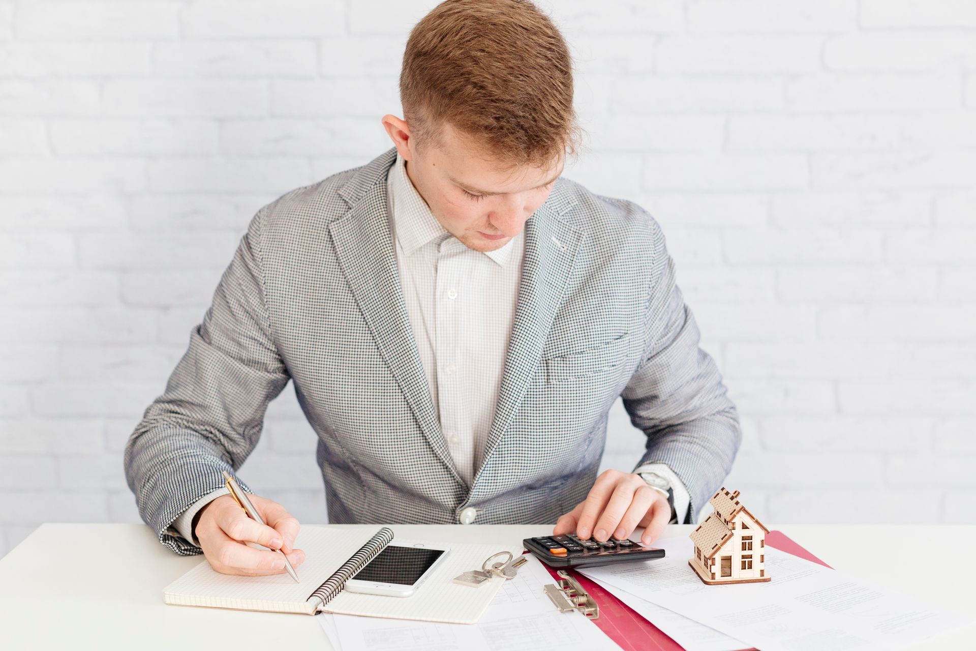 A man is sitting at a table using a calculator and writing in a notebook.