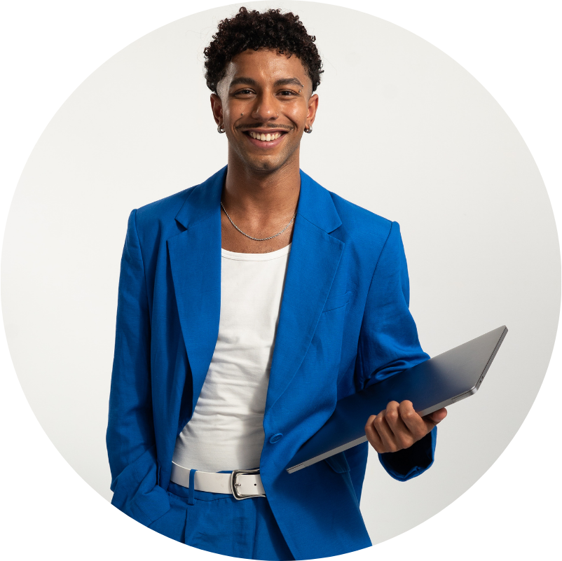 Man in blue suit smiles, holding a laptop against a white background.