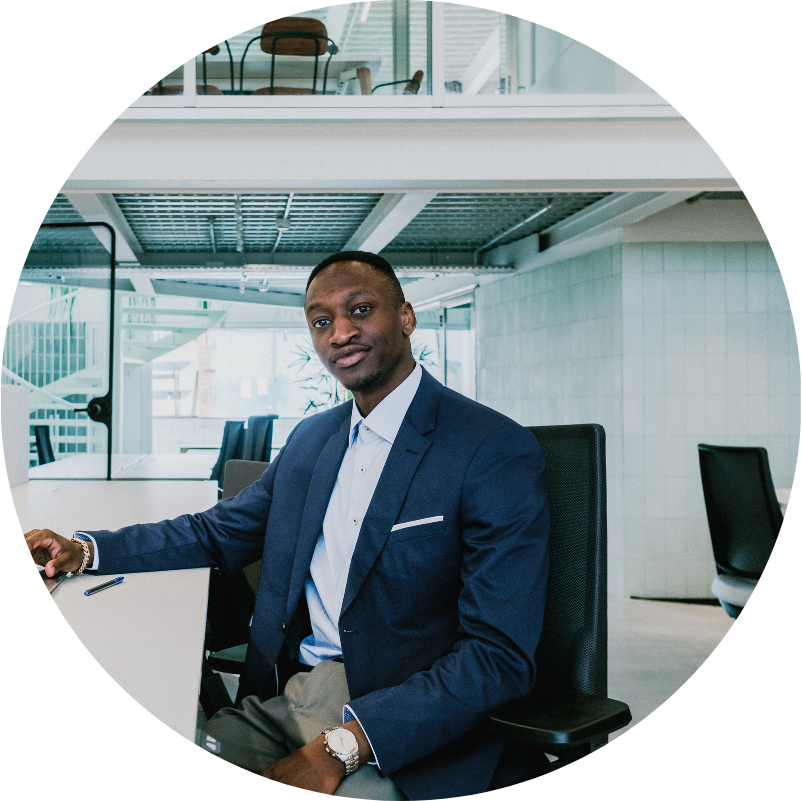 Black man in a suit sits at a desk in a modern office, looking at the camera.