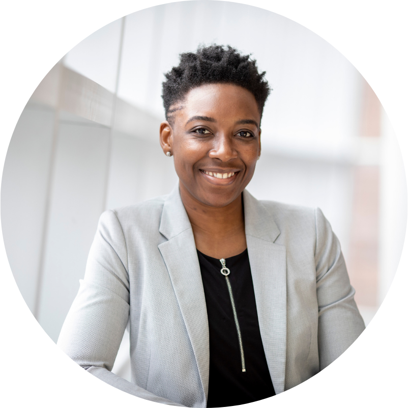 Smiling Black woman in gray blazer, black shirt, short dark hair, near window.