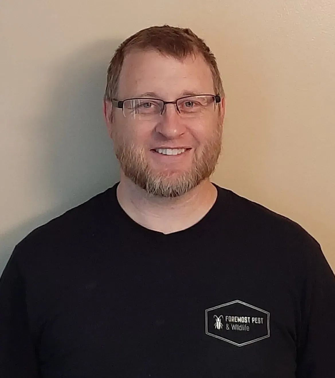 Man with glasses and beard smiles, wearing a black t-shirt with a logo.