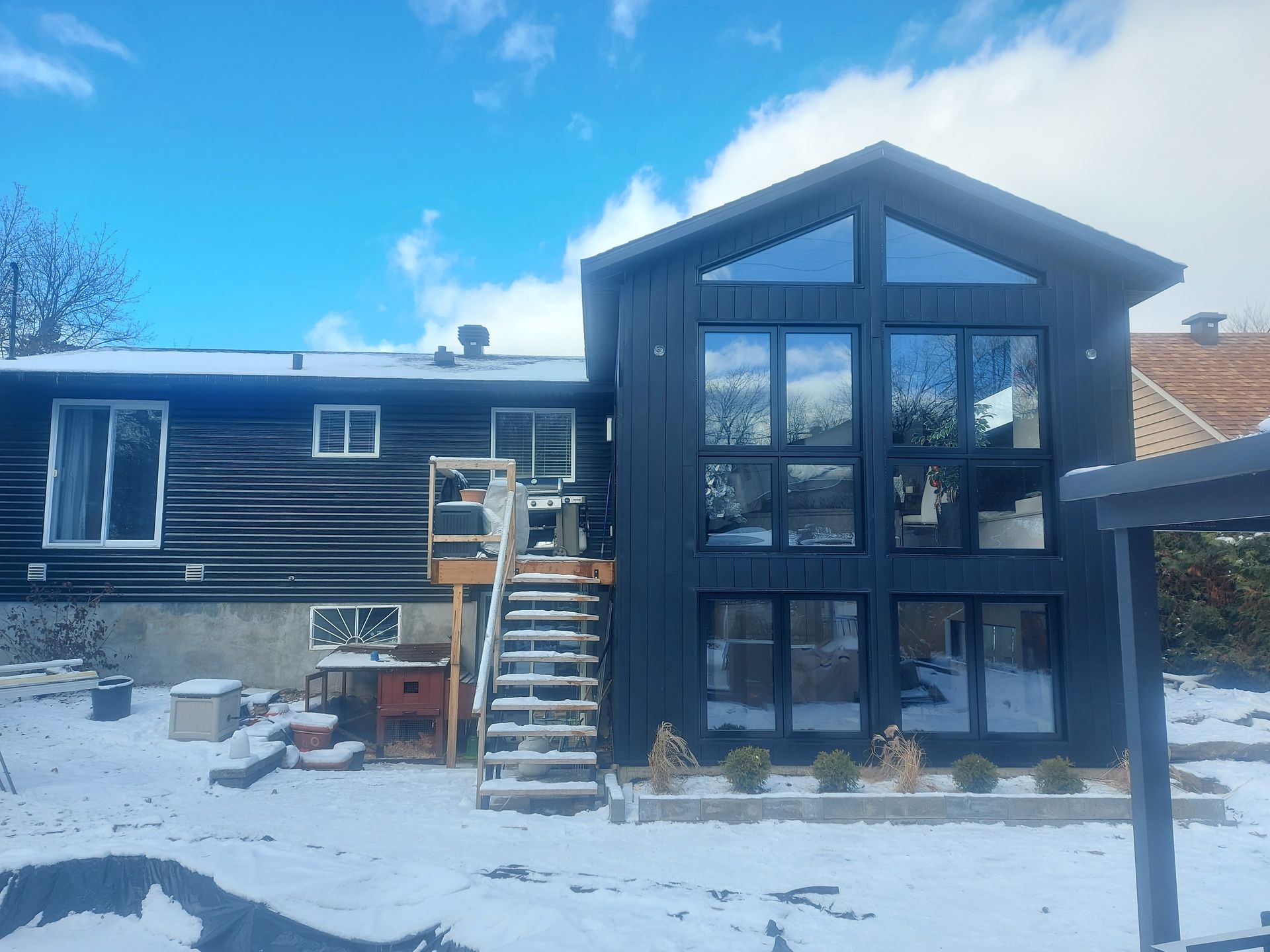 Une grande maison noire avec beaucoup de fenêtres est recouverte de neige.