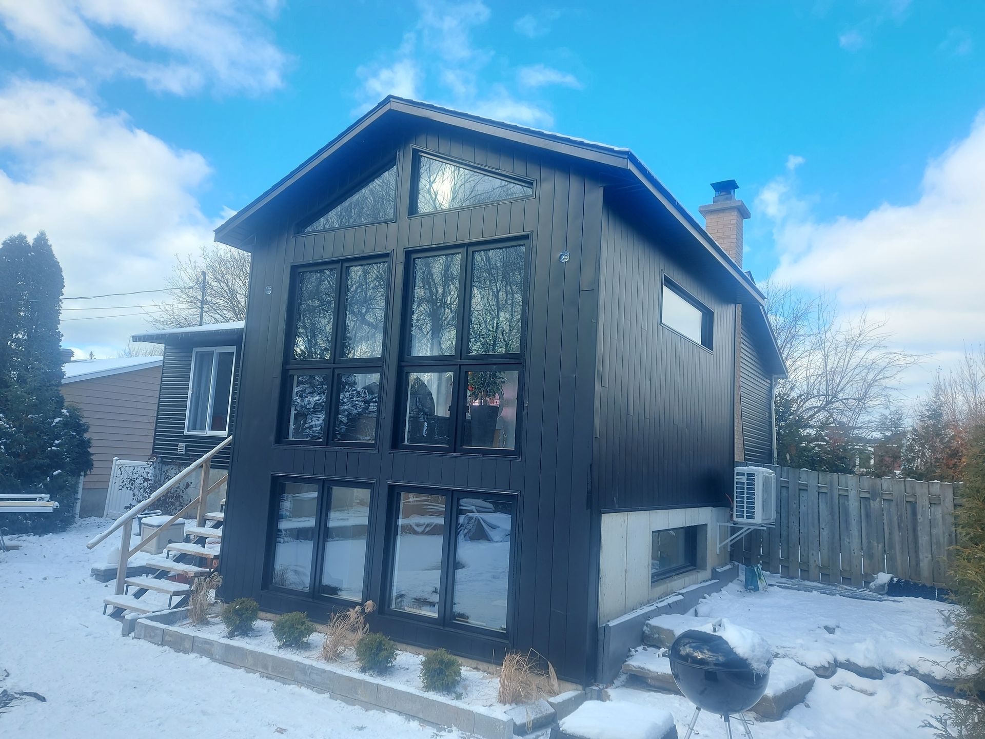 Une grande maison noire avec beaucoup de fenêtres est recouverte de neige.
