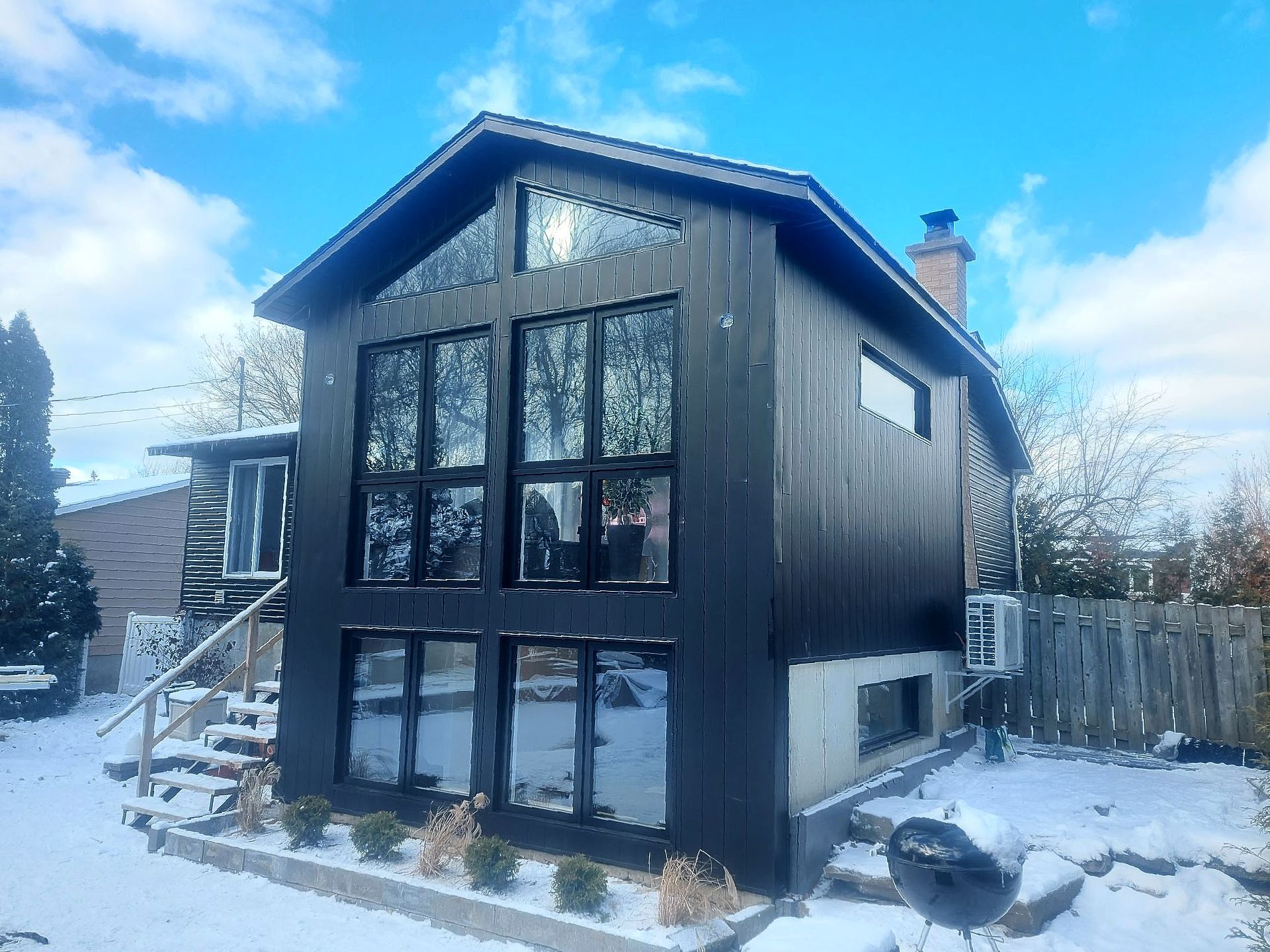 Une maison noire avec beaucoup de fenêtres est couverte de neige