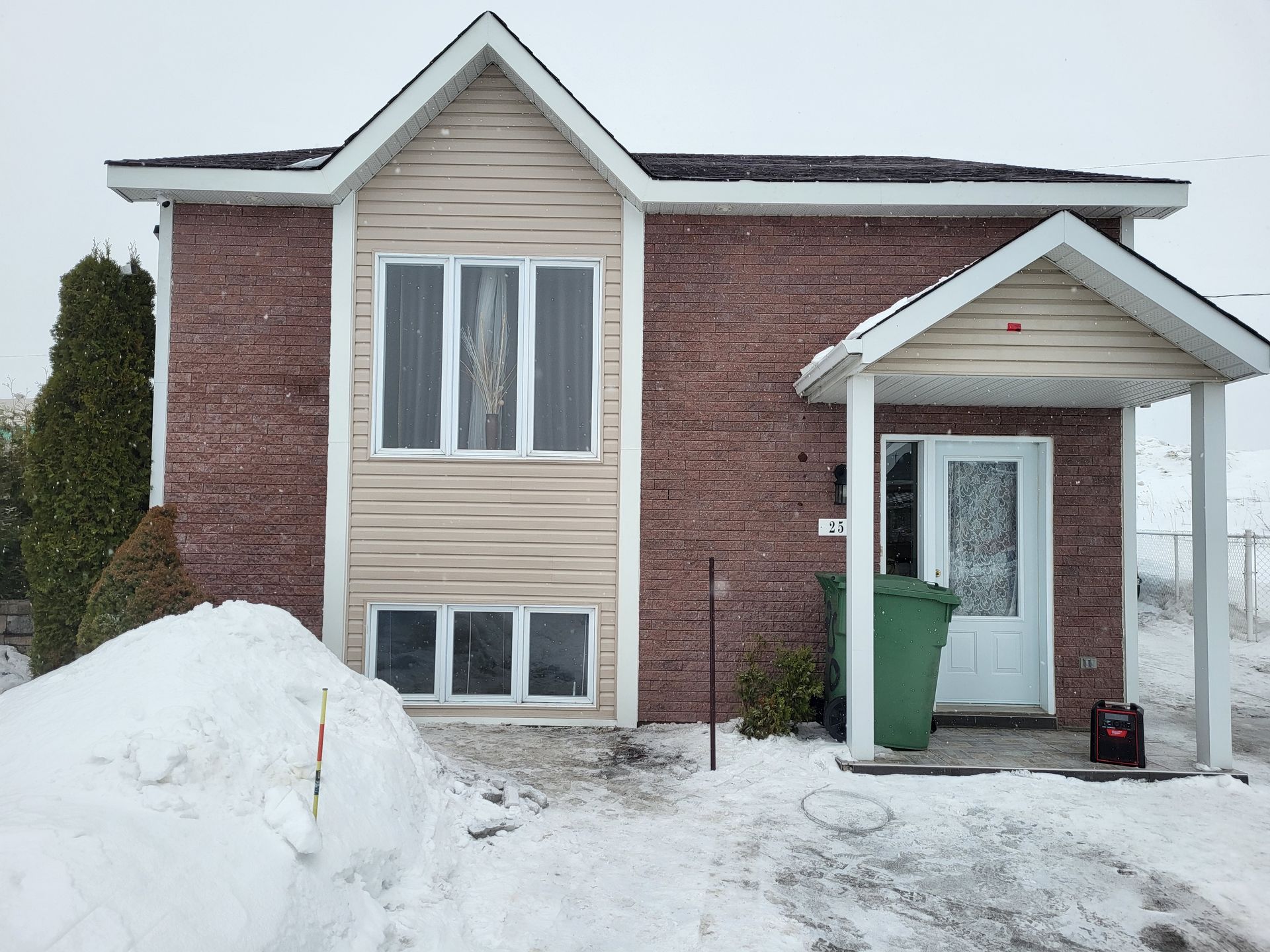 Une maison en briques avec une poubelle verte devant