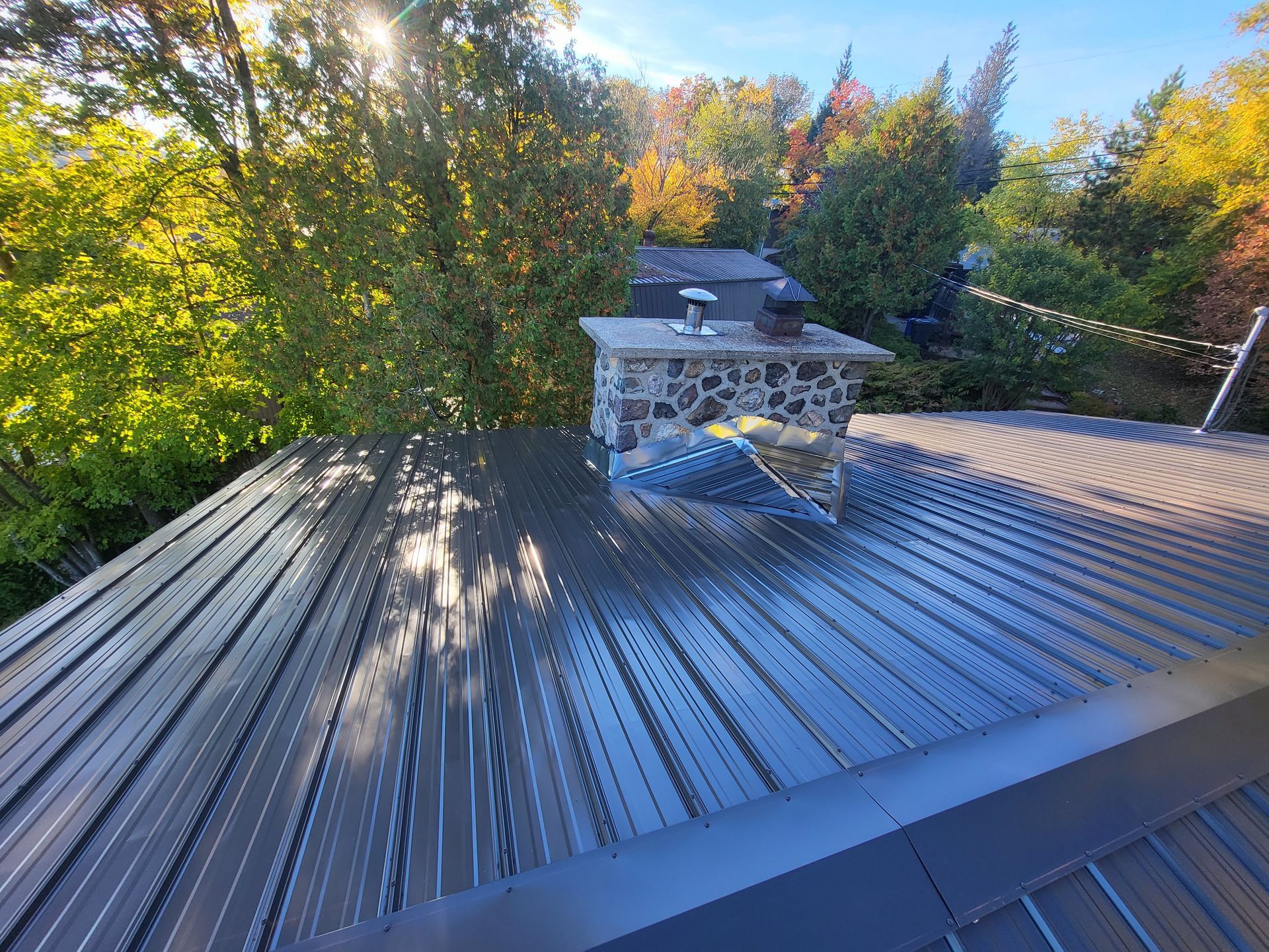 Un toit avec une cheminée dessus et des arbres en arrière-plan.