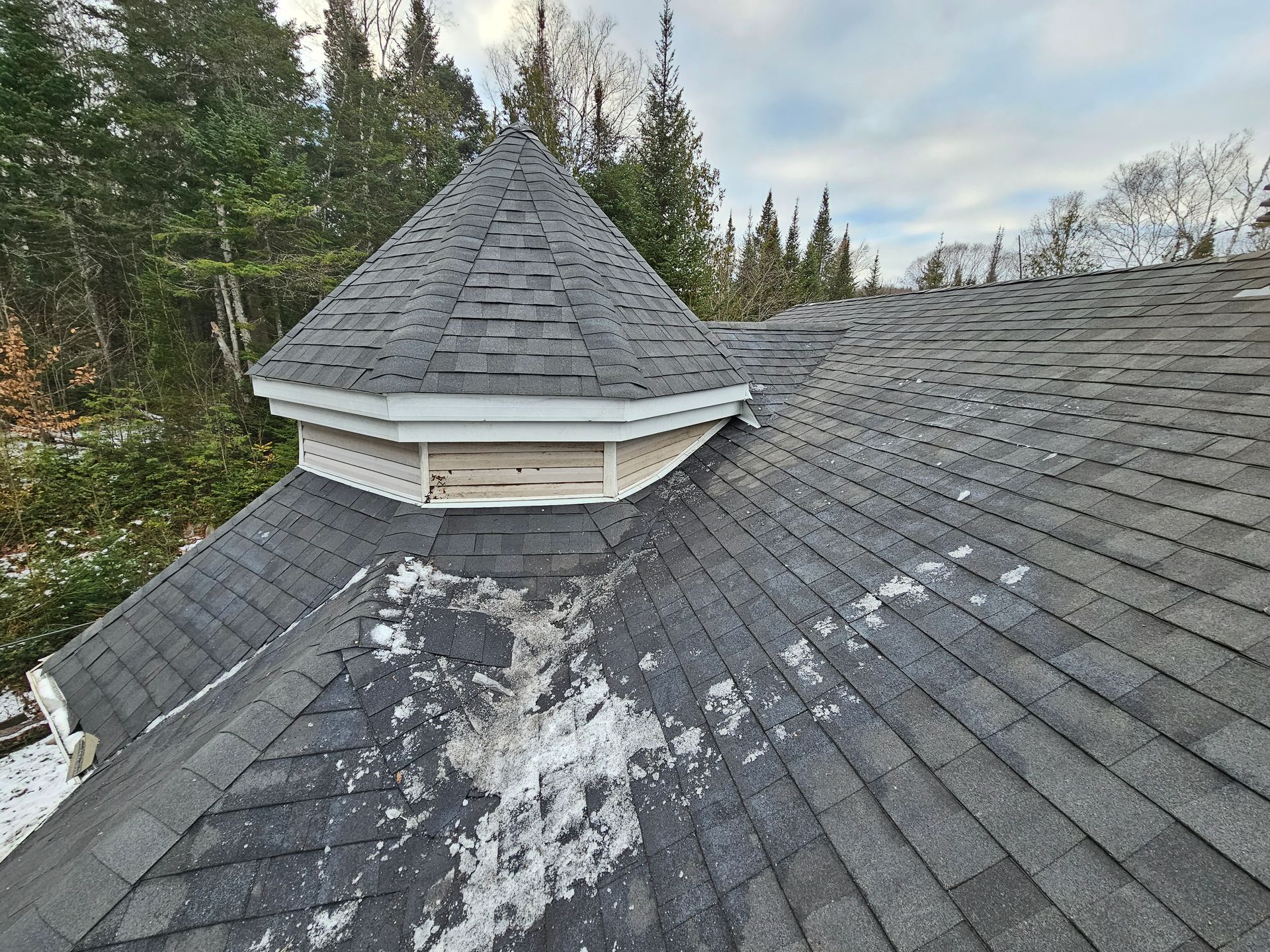 Un toit avec de la neige dessus et des arbres en arrière-plan.