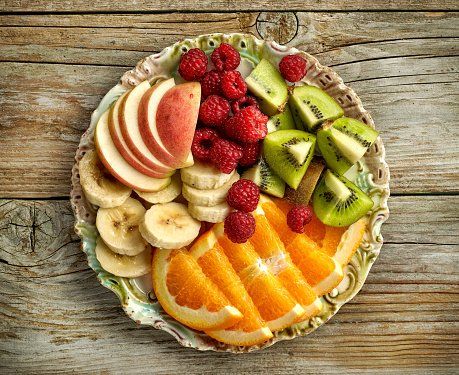 Wooden plate of sliced apples, oranges, bananas, strawberries, and kiwis. 