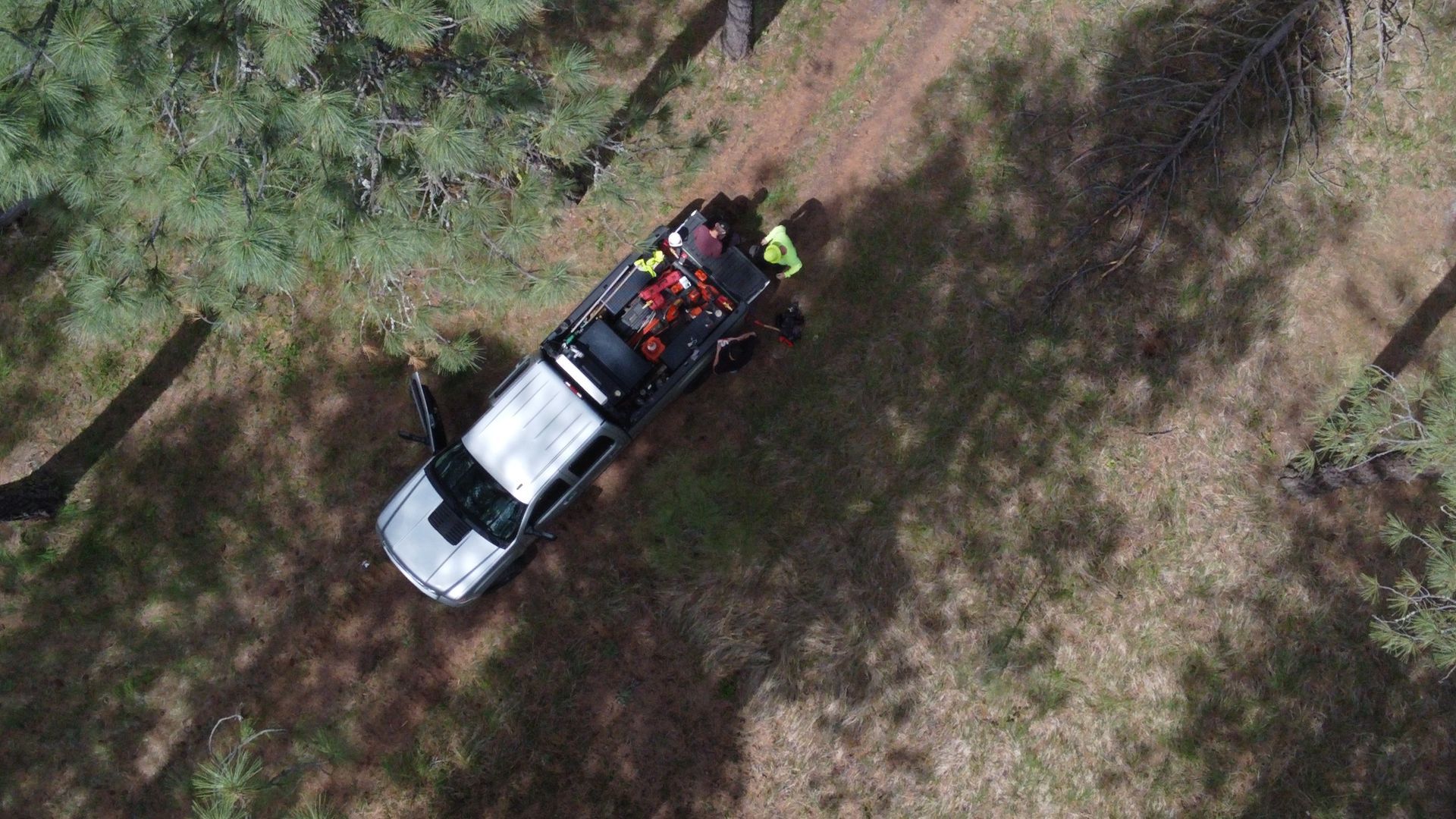 An aerial view of a truck driving down a dirt road in the woods.