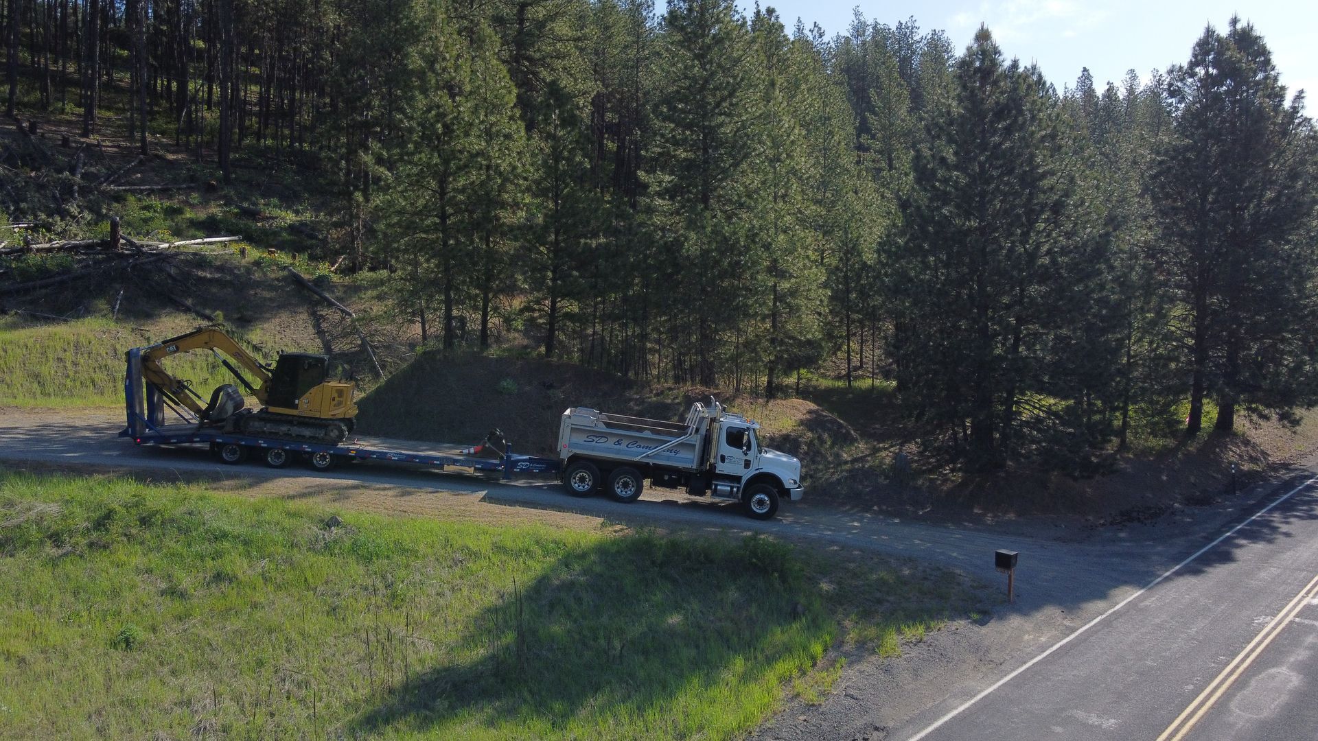 A dump truck is driving down a dirt road next to a forest.