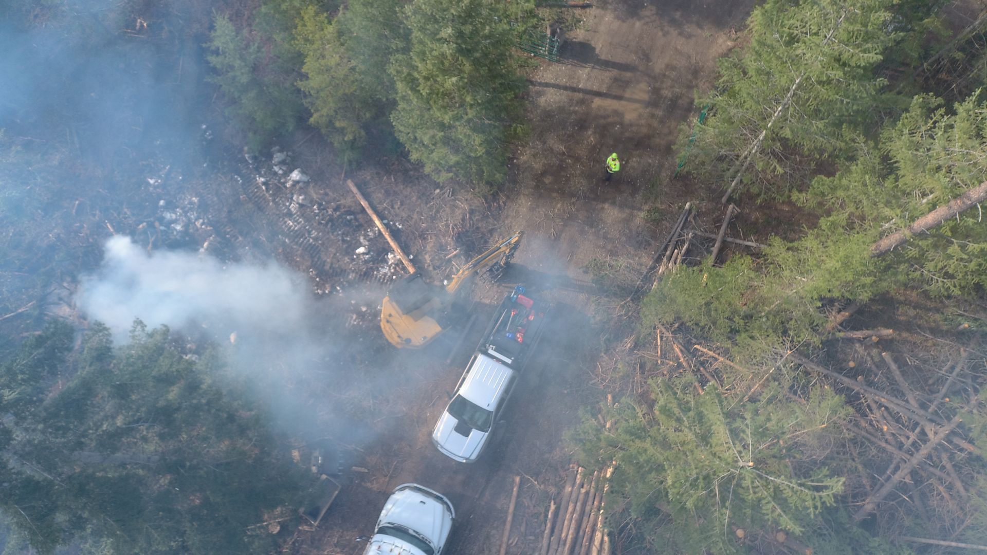 An aerial view of a forest fire with smoke coming out of the trees.