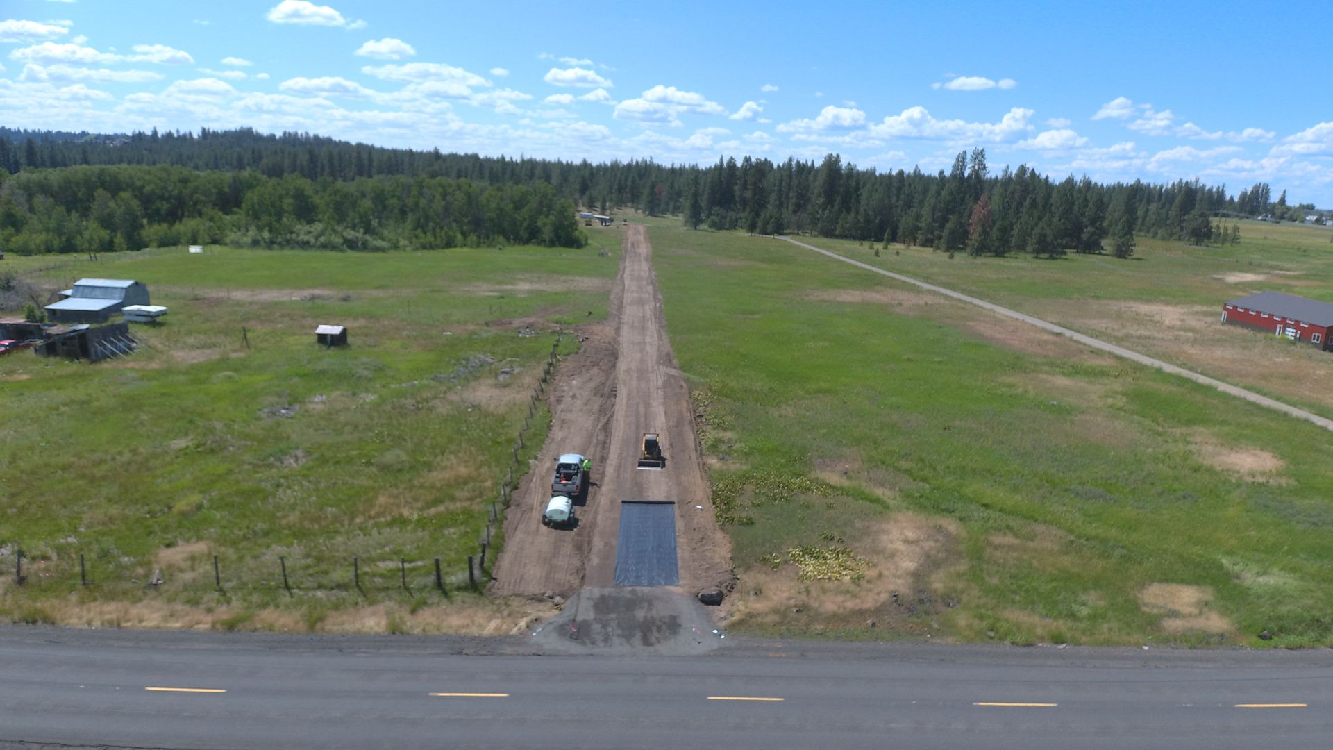 An aerial view of a truck driving down a dirt road next to a field.