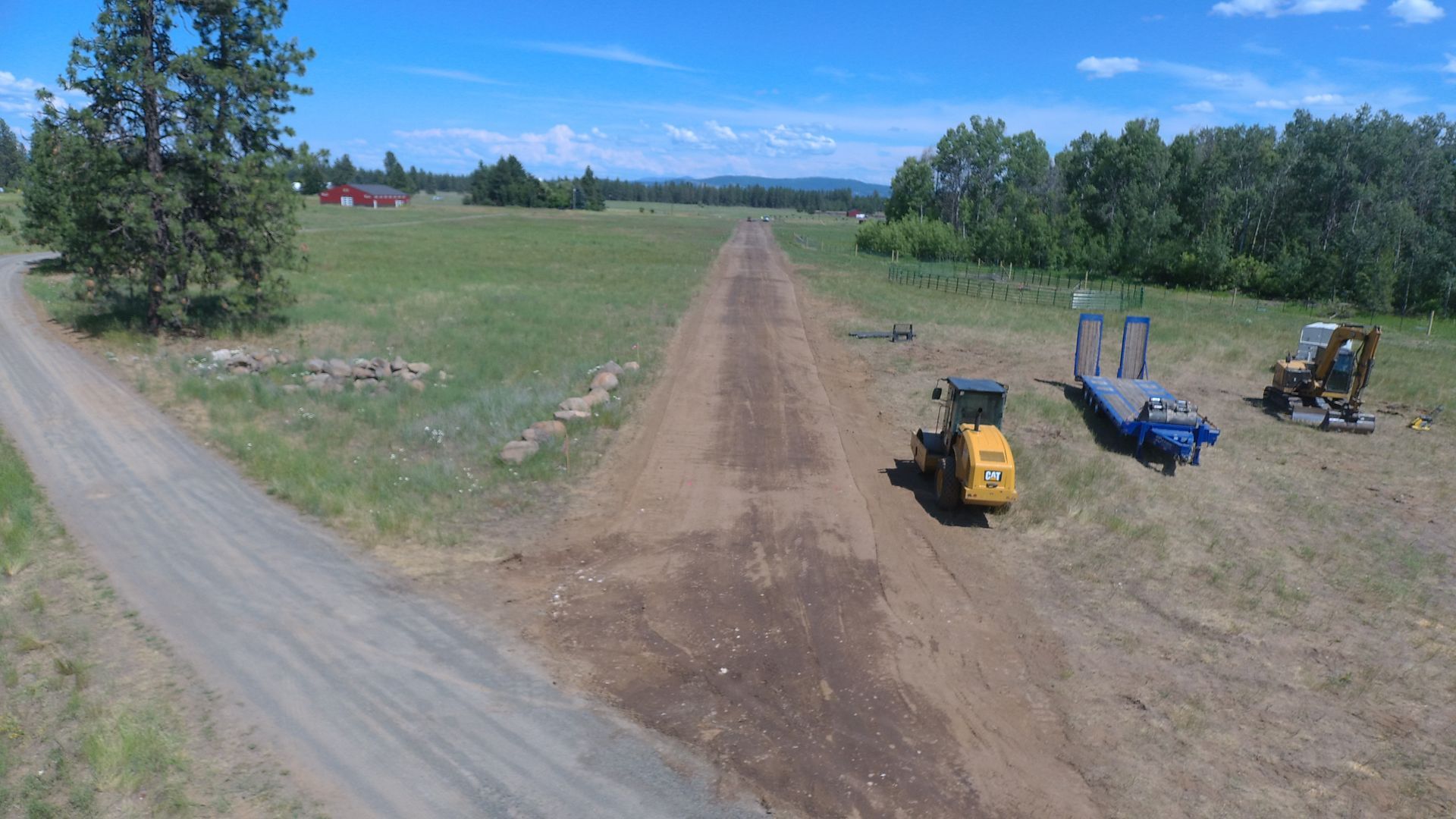 A tractor is driving down a dirt road next to a trailer.