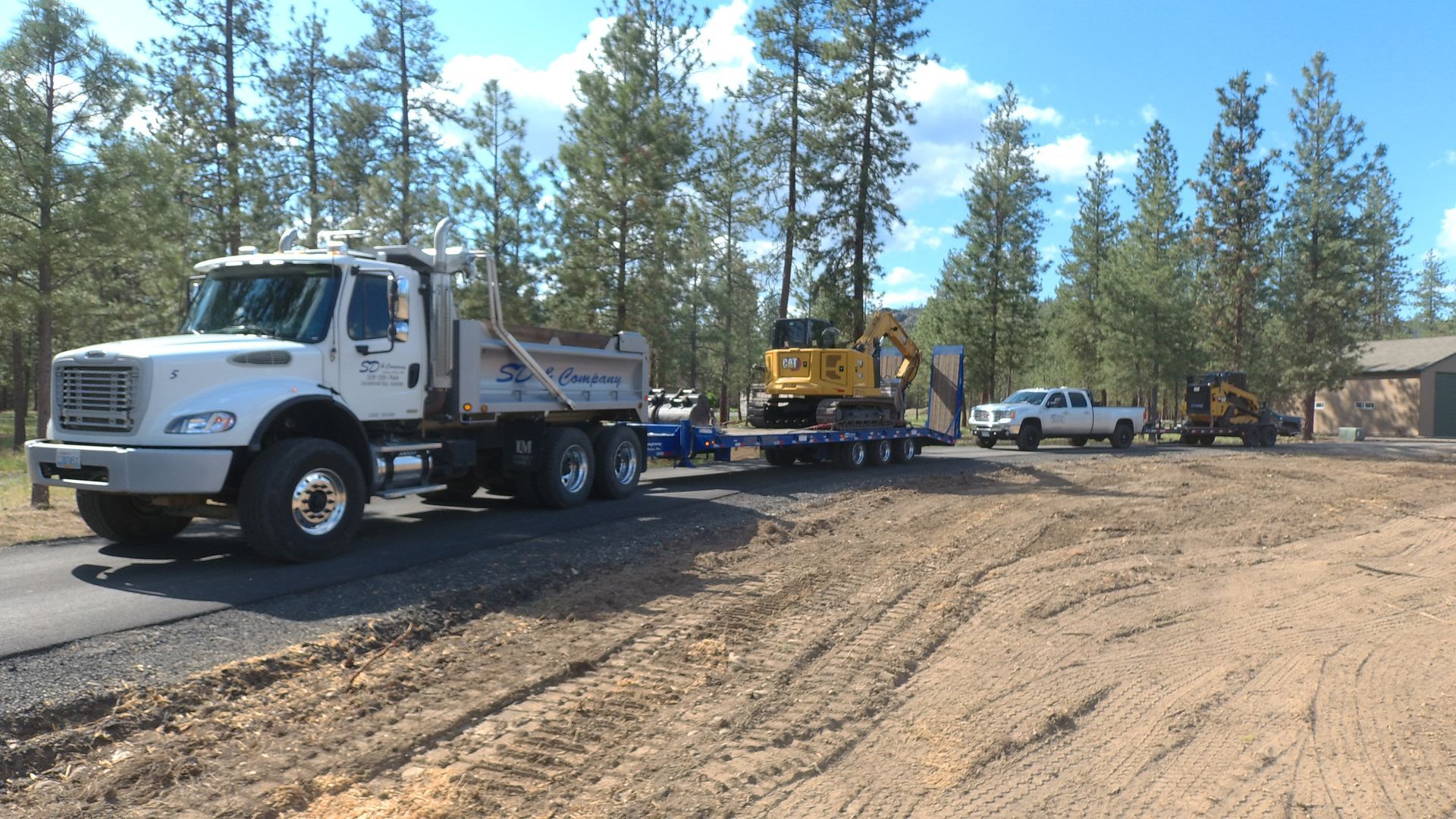 A dump truck is driving down a dirt road with trees in the background.