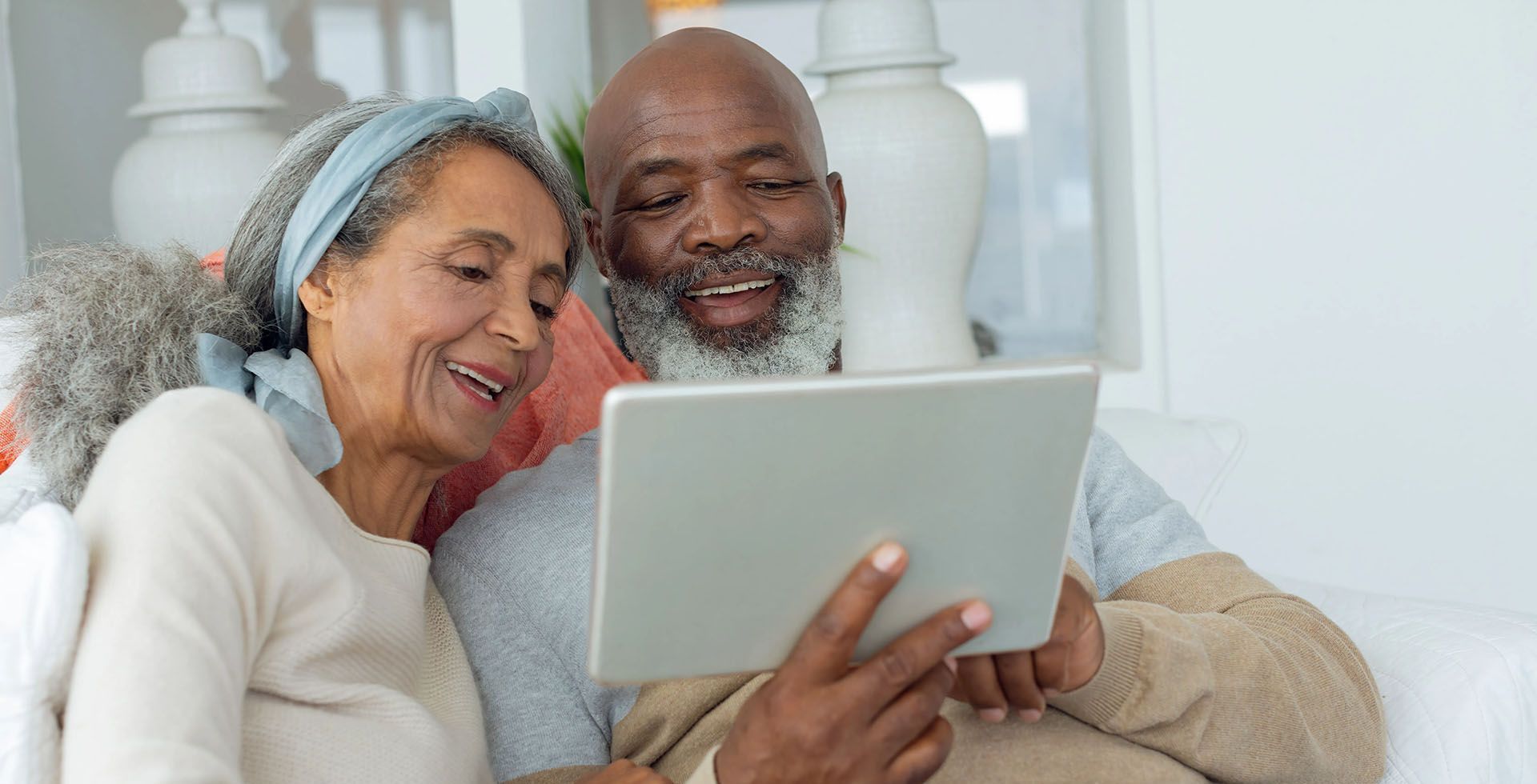 an elderly couple is sitting on a couch looking at a tablet .