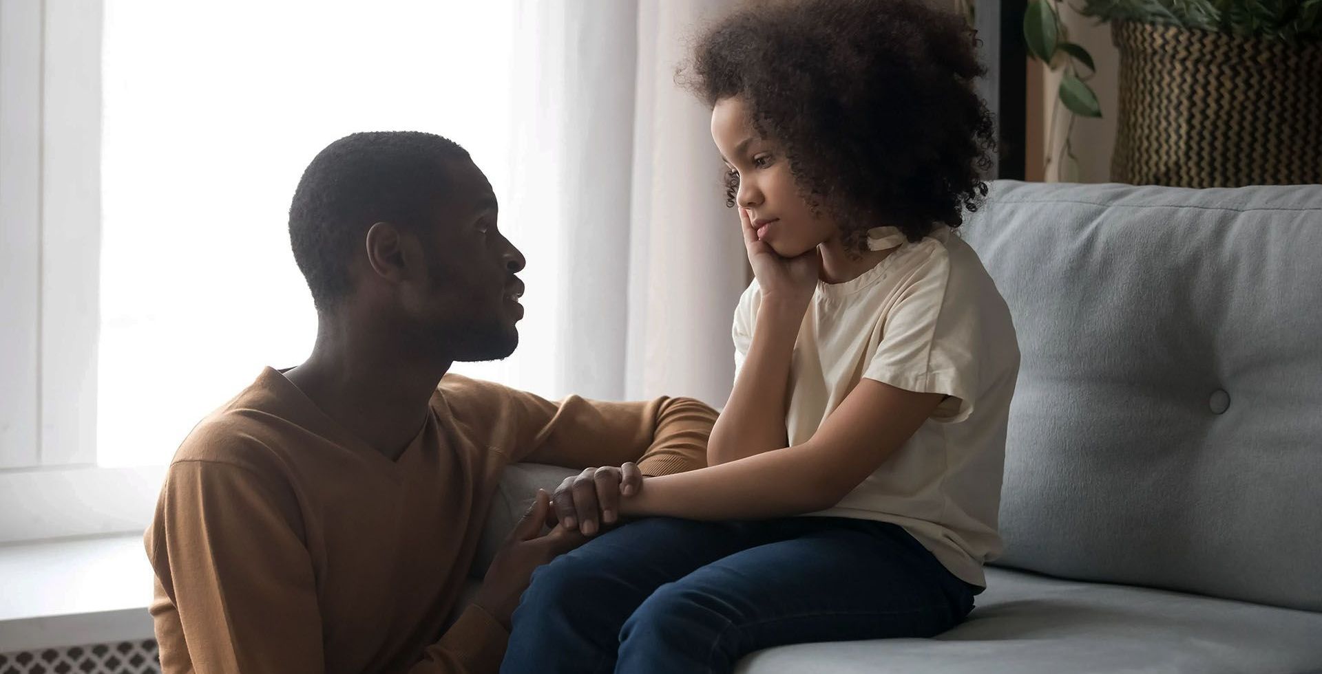 a man and a little girl are sitting on a couch talking to each other .