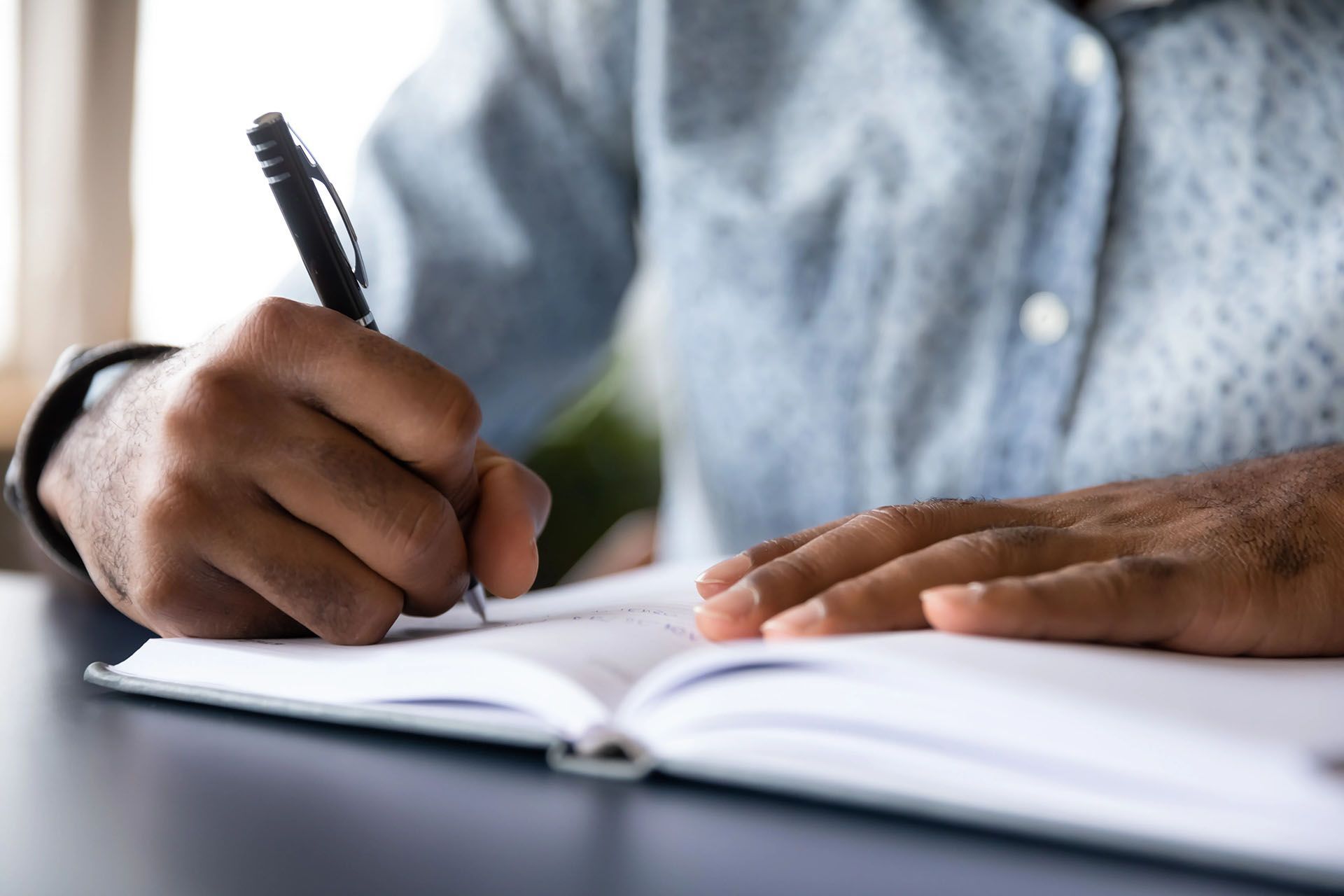 a man is writing in a notebook with a pen .