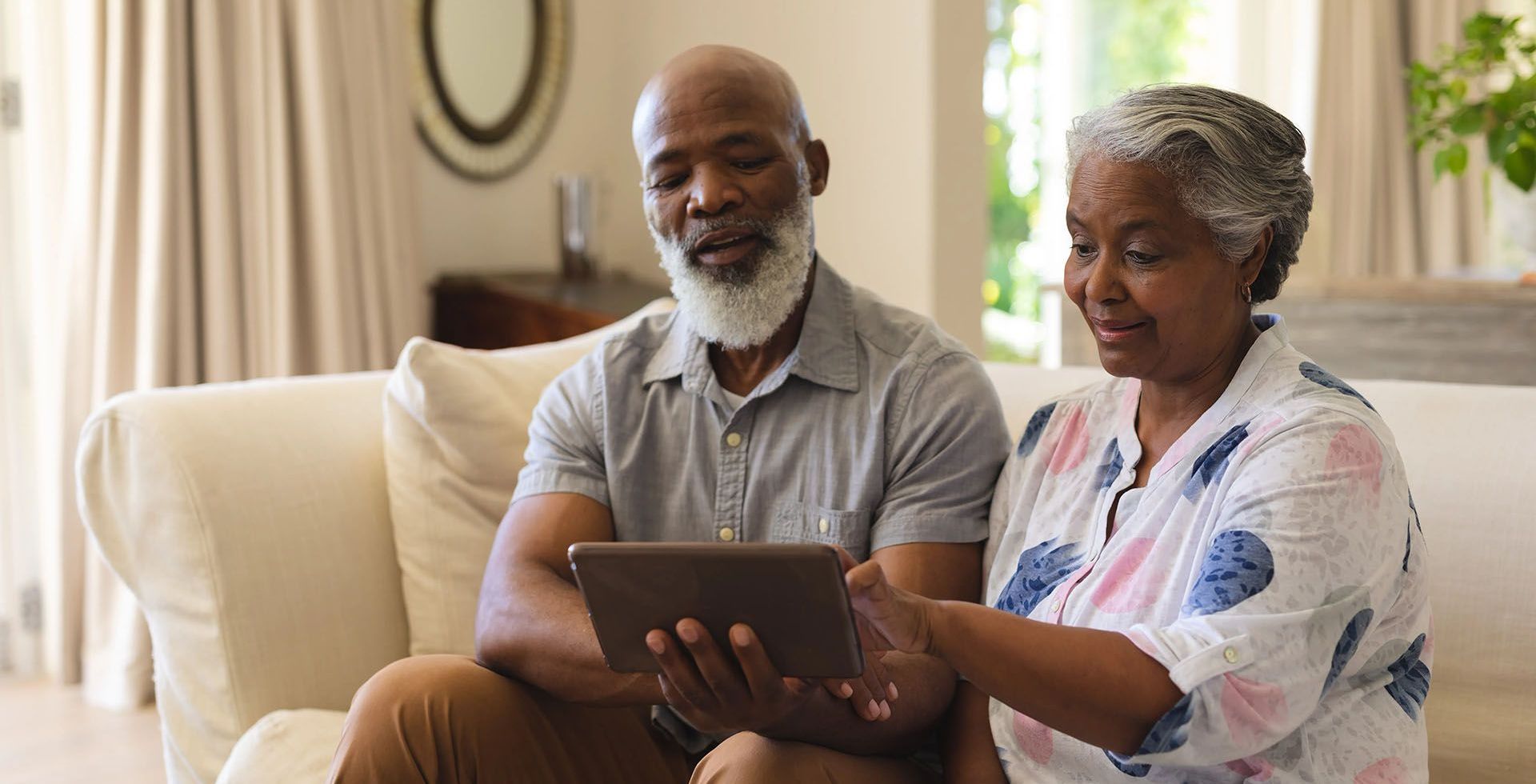 an elderly couple is sitting on a couch looking at a tablet .