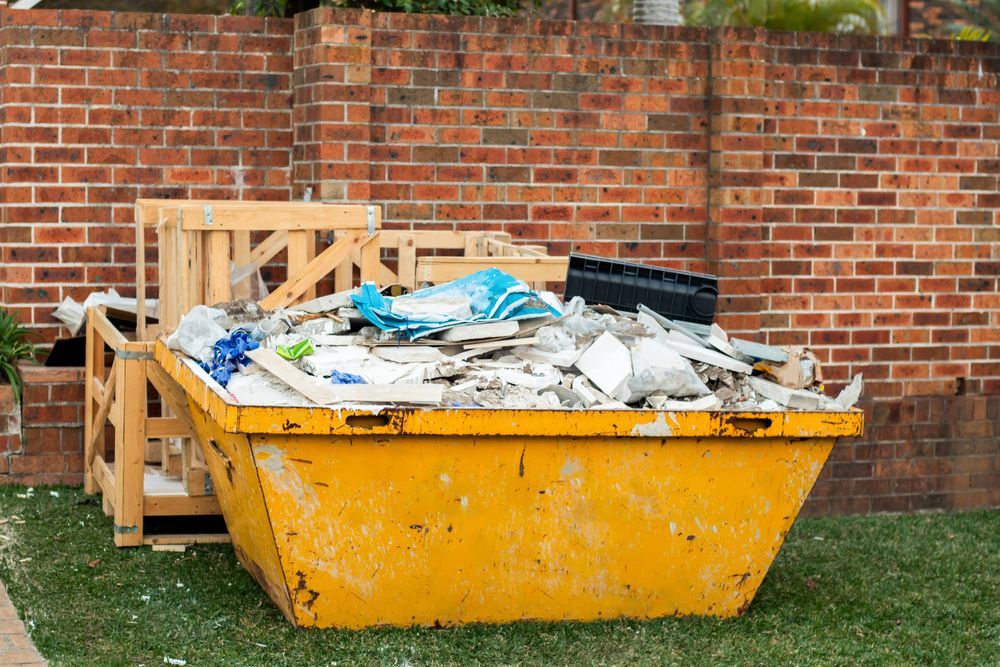 A Yellow Dumpster Filled With Trash Is Sitting In Front Of A Brick Wall — Green Solutions Qld Pty Ltd in Mulara, QLD