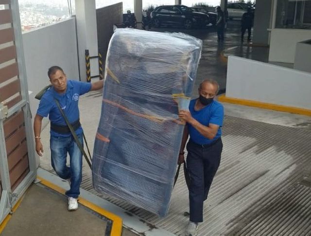 Dos hombres llevan un objeto grande envuelto en plástico.