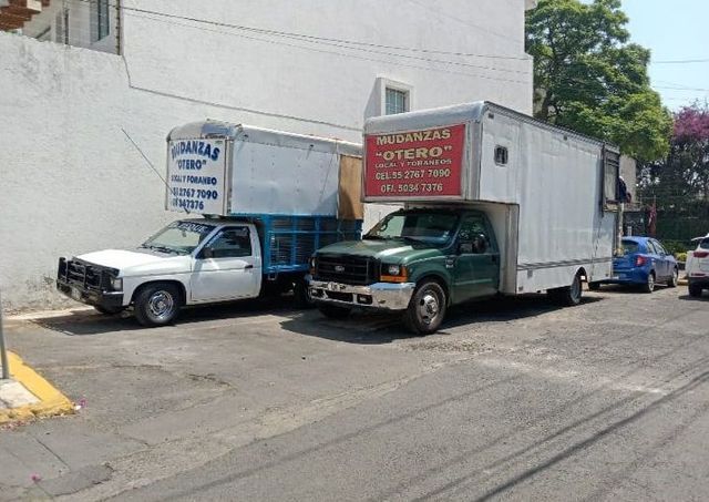 Dos camiones de mudanzas están estacionados uno al lado del otro al costado de la carretera.