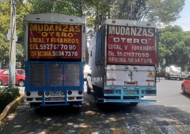 Dos camiones de mudanzas están estacionados al costado de la carretera.