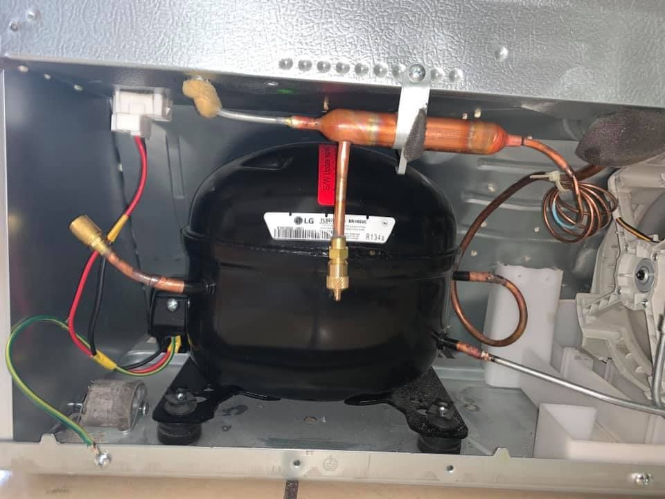 The inside of a refrigerator with a compressor and wires