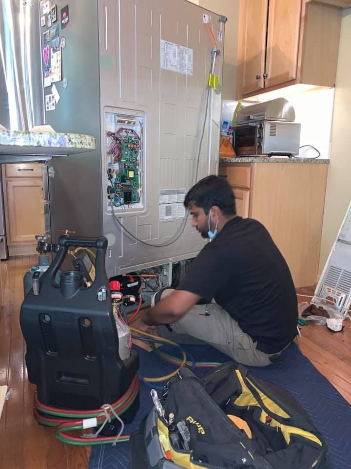 a man is sitting on the floor fixing a refrigerator .