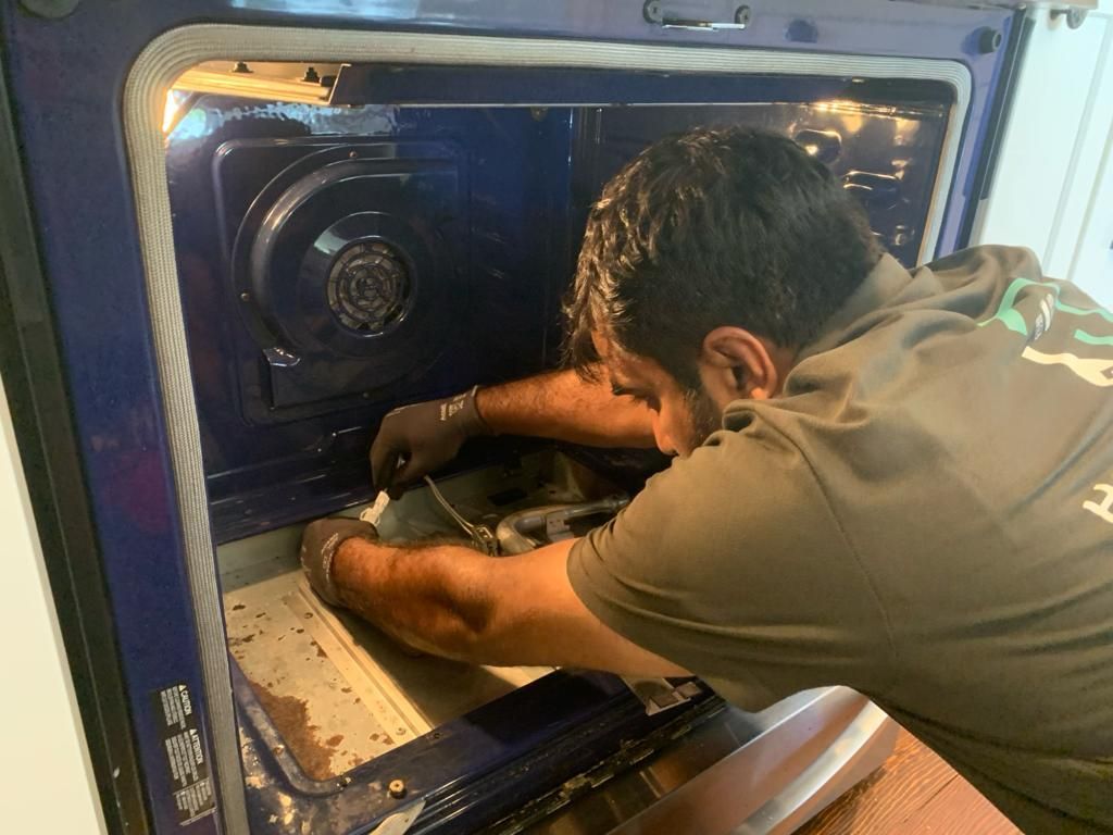 A man is working on an oven with a screwdriver.