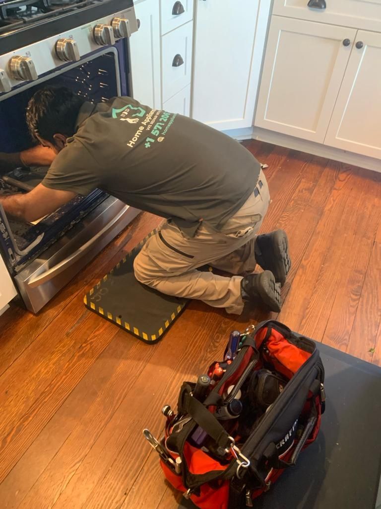 A man is kneeling on the floor fixing an oven in a kitchen.