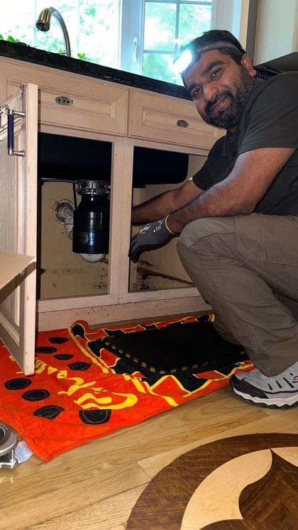 Man working under a kitchen sink, wearing a headlamp.