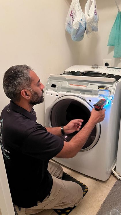A person using a screwdriver to repair a washing machine in a laundry room.