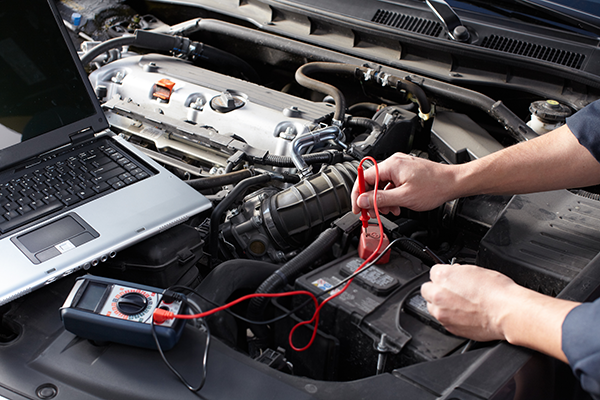 A person is working on a car with a laptop in the background.