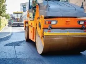 A yellow and brown road roller is driving down a street.