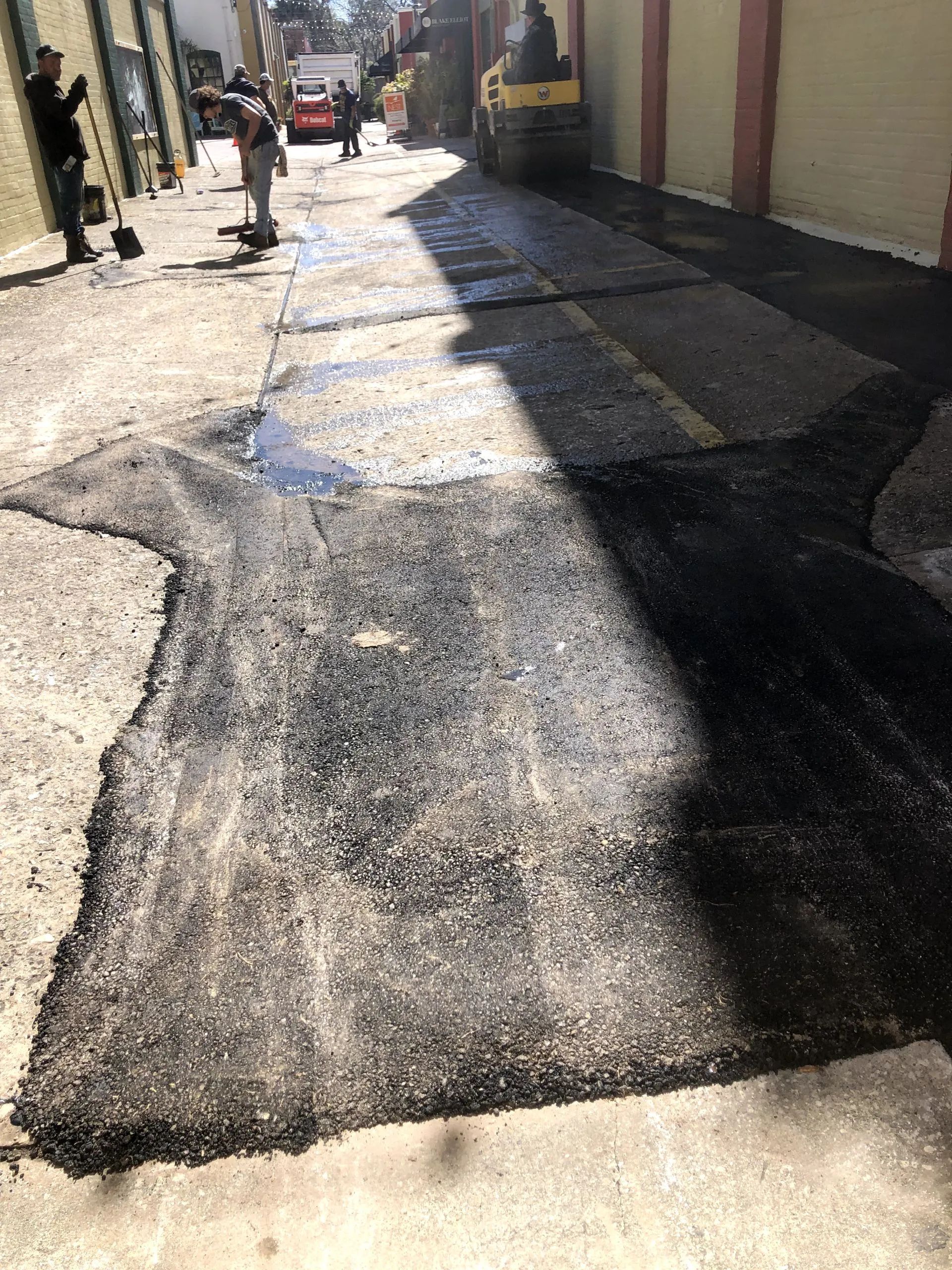 A man is laying asphalt on a sidewalk in a parking lot.