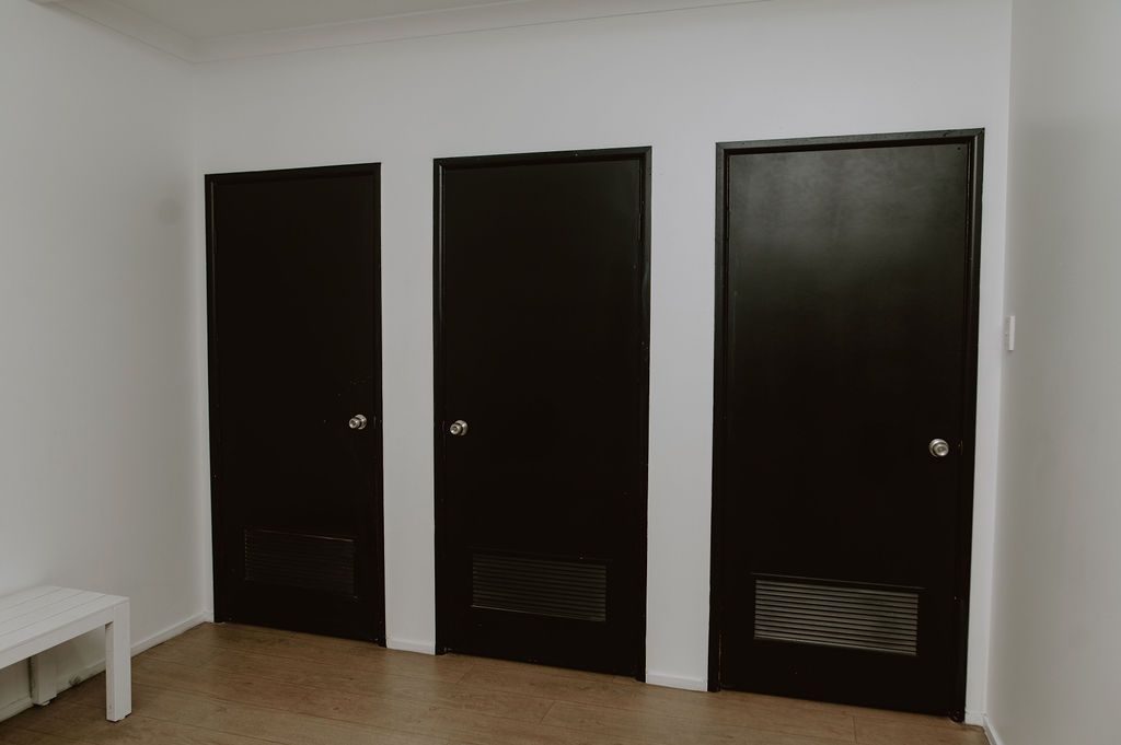 Three identical black doors with ventilation grates at the bottom stand side-by-side against a plain white wall.