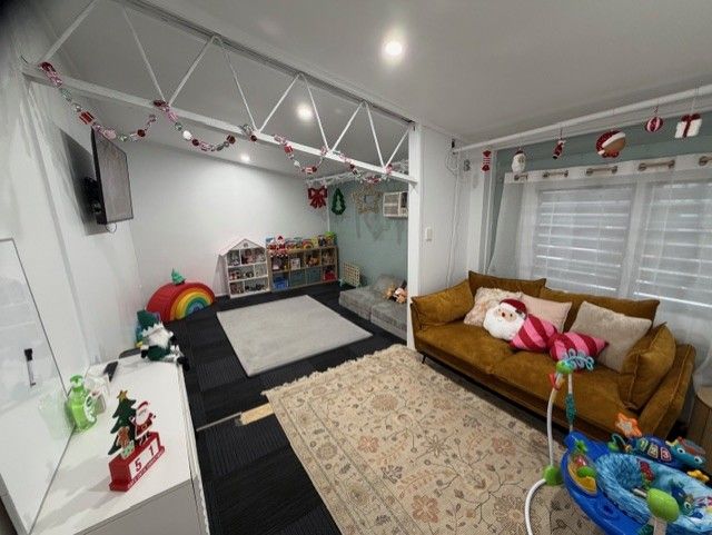 A cozy, festive living area with a brown sofa, area rugs, a child's play space, and Christmas decorations.