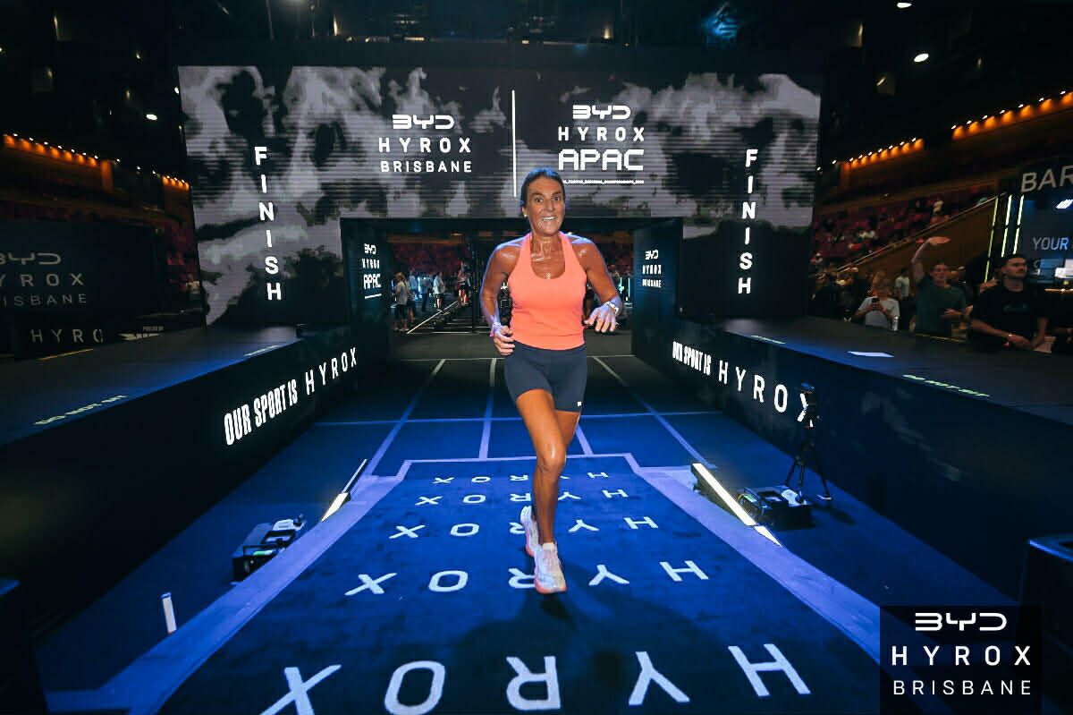 Runner in orange top on HYROX competition track under bright arena lights