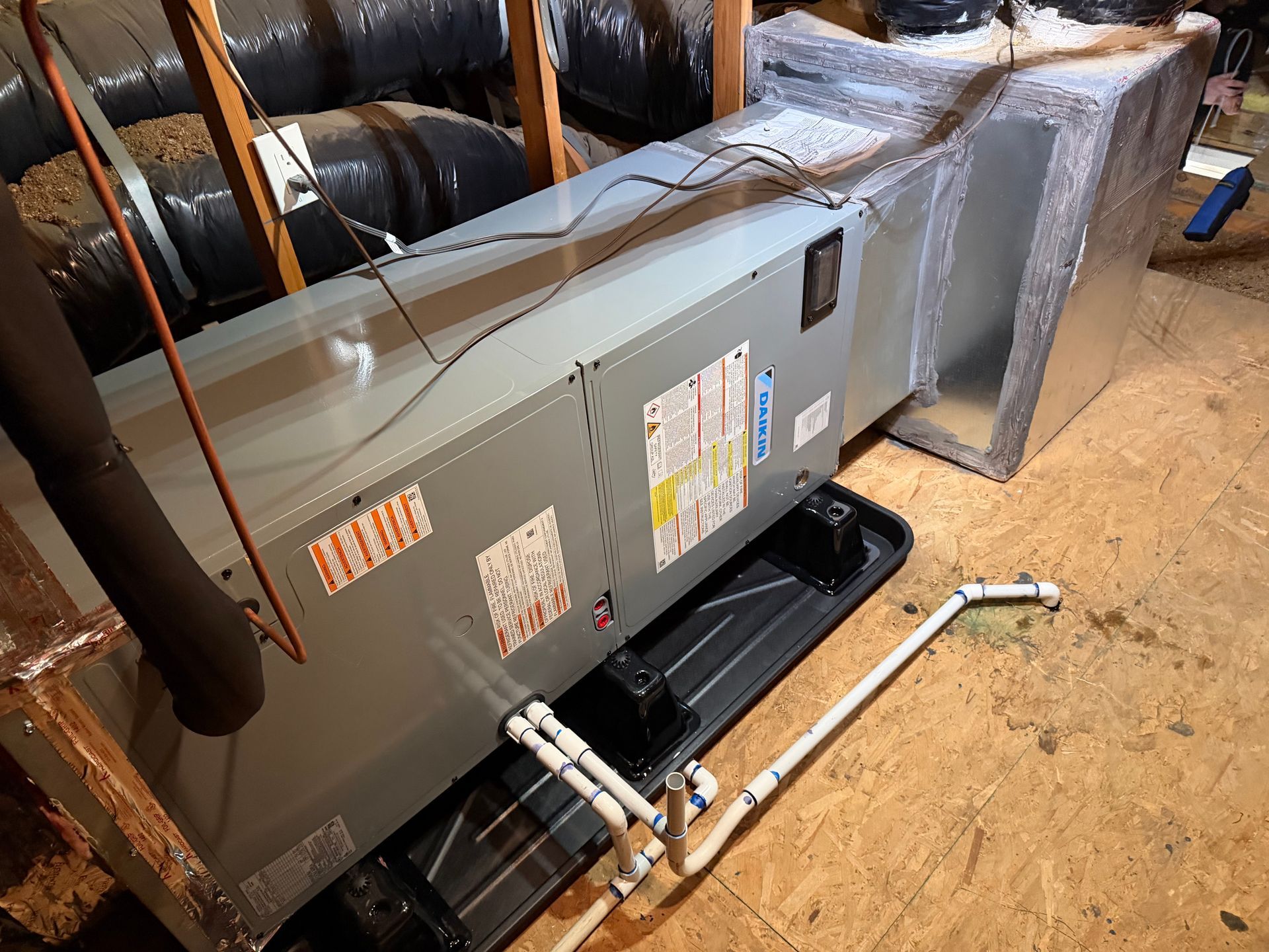 Large gray HVAC unit with exposed pipes in a basement or utility room