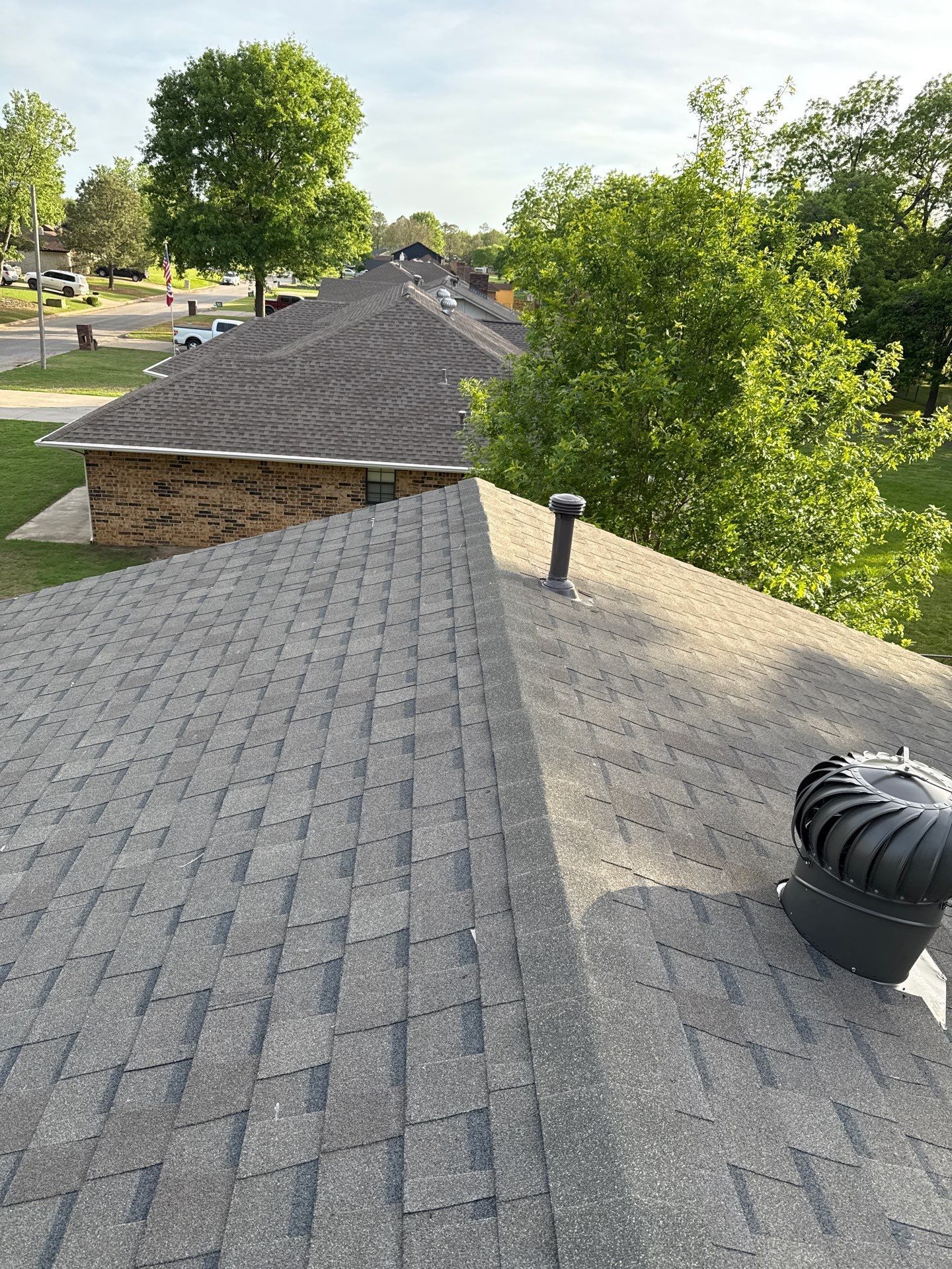 The roof of a house with a fan on it and trees in the background.