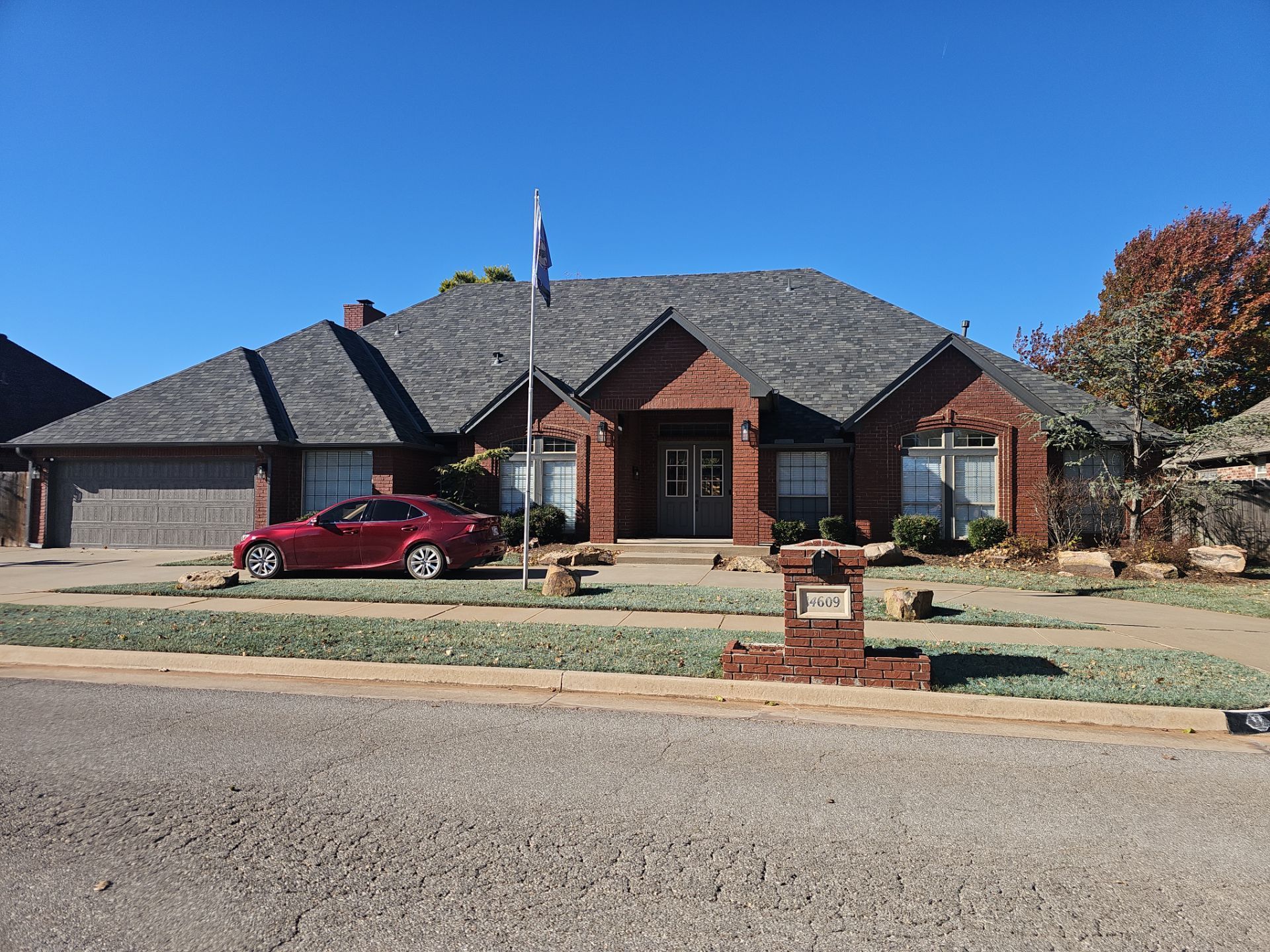 A red car is parked in front of a large brick house