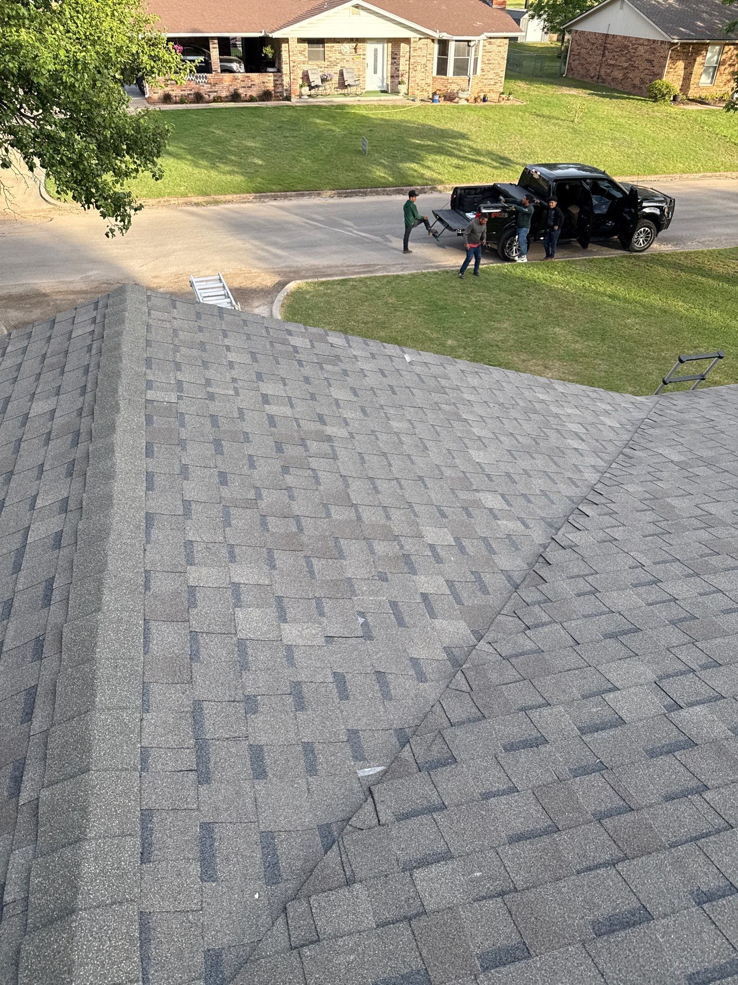 View from a roof, focusing on asphalt shingles; a truck with people outside is parked on the street.