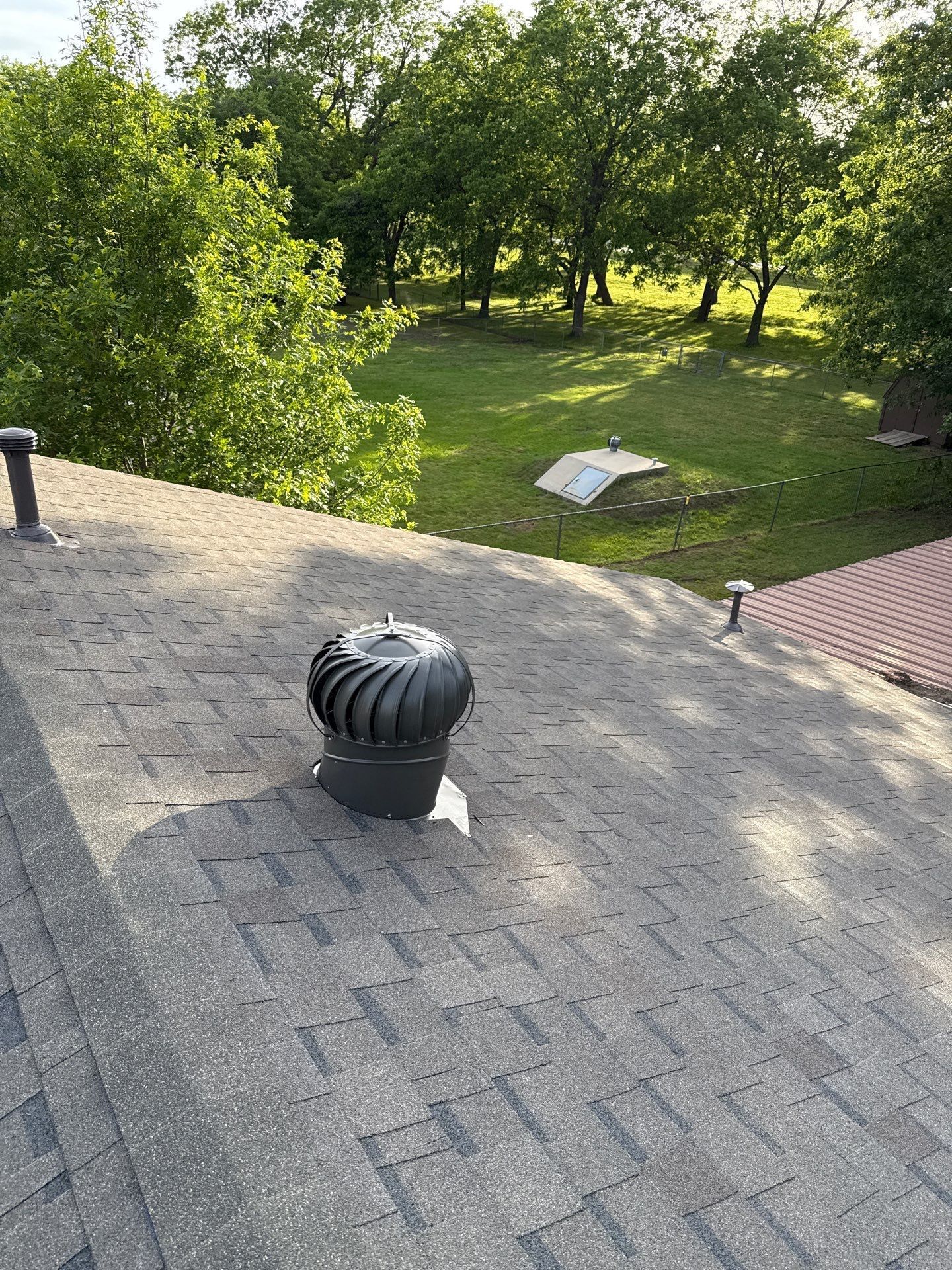 A roof with a wind turbine on it and trees in the background.