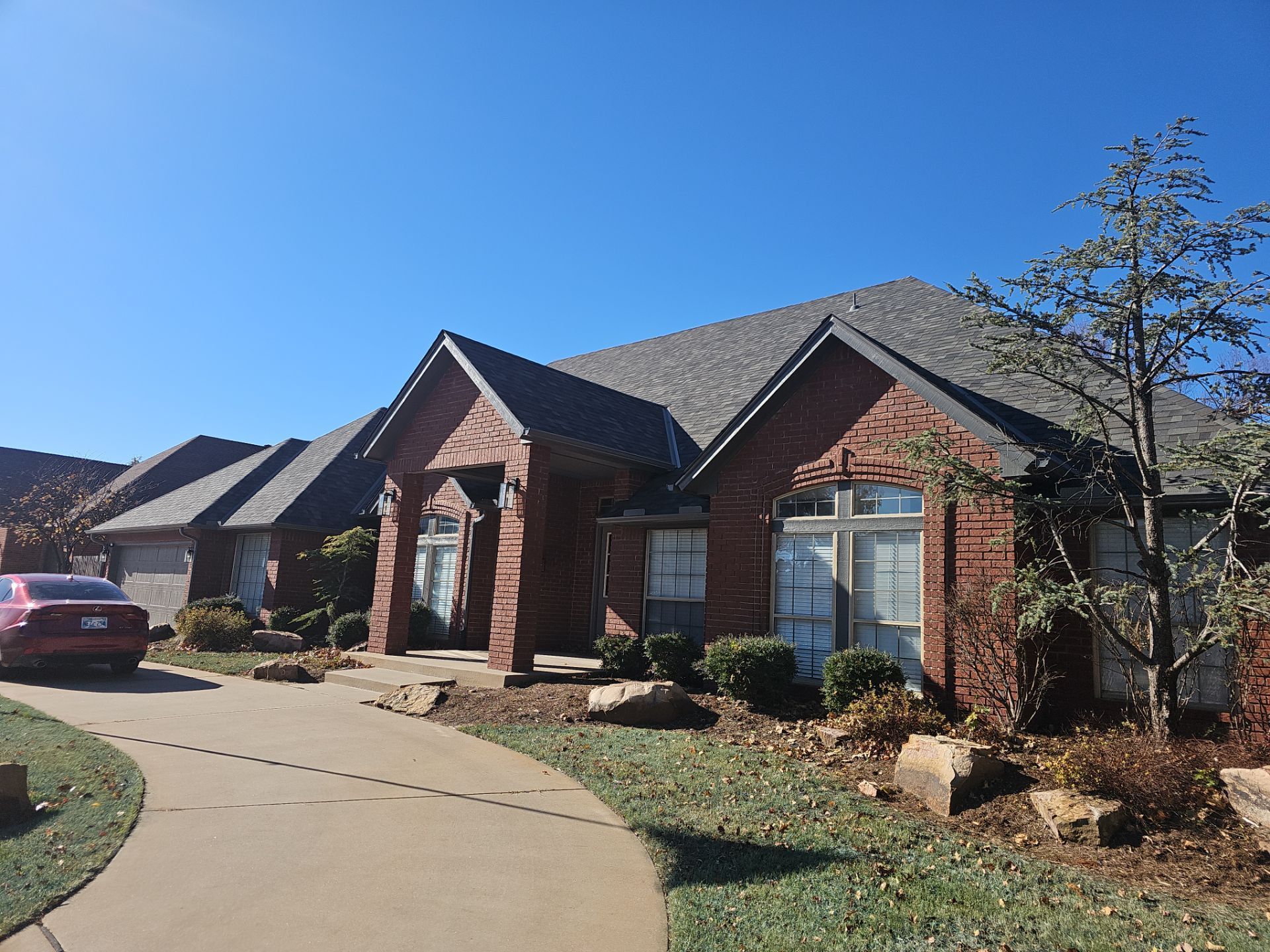 A red car is parked in front of a large brick house